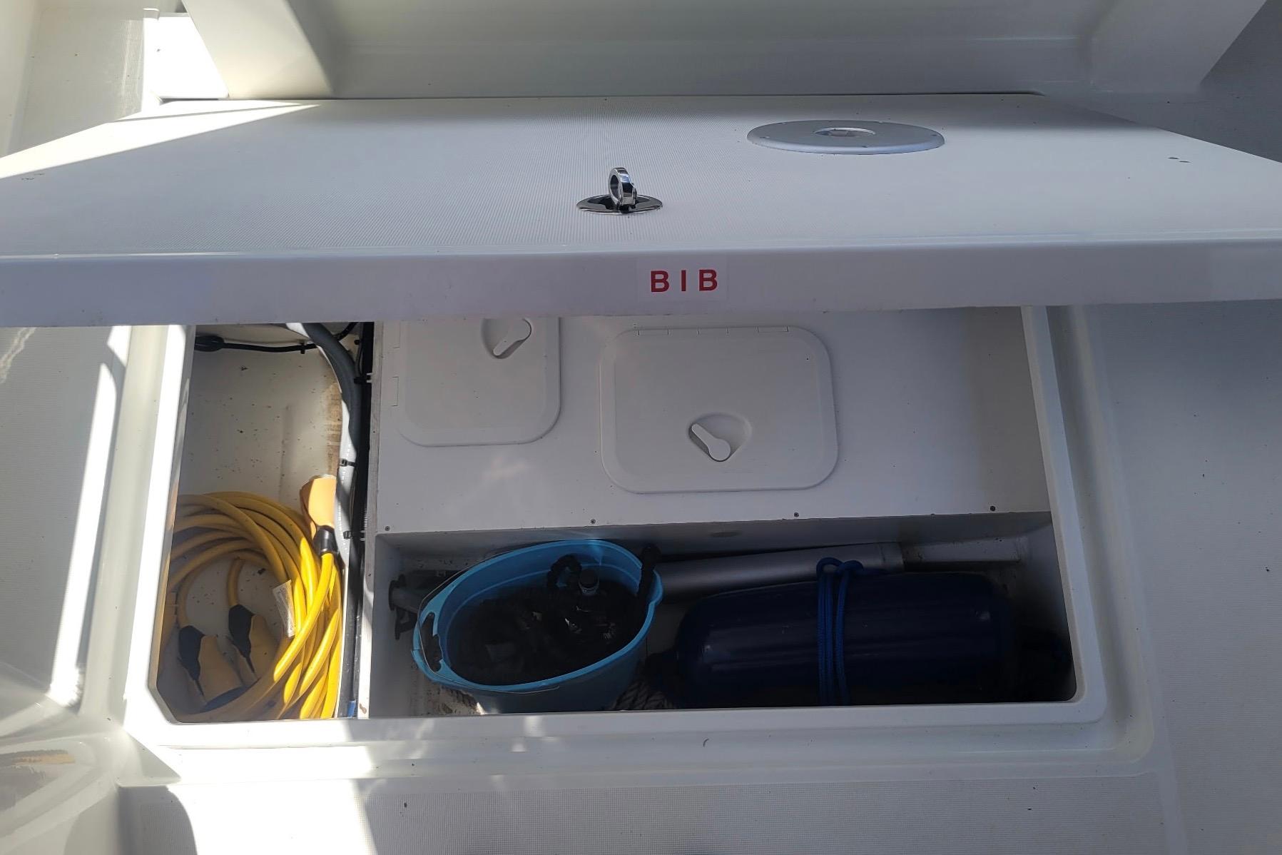 Storage compartment on a 2019 Beneteau Antares 23 boat, containing a hose and bucket.