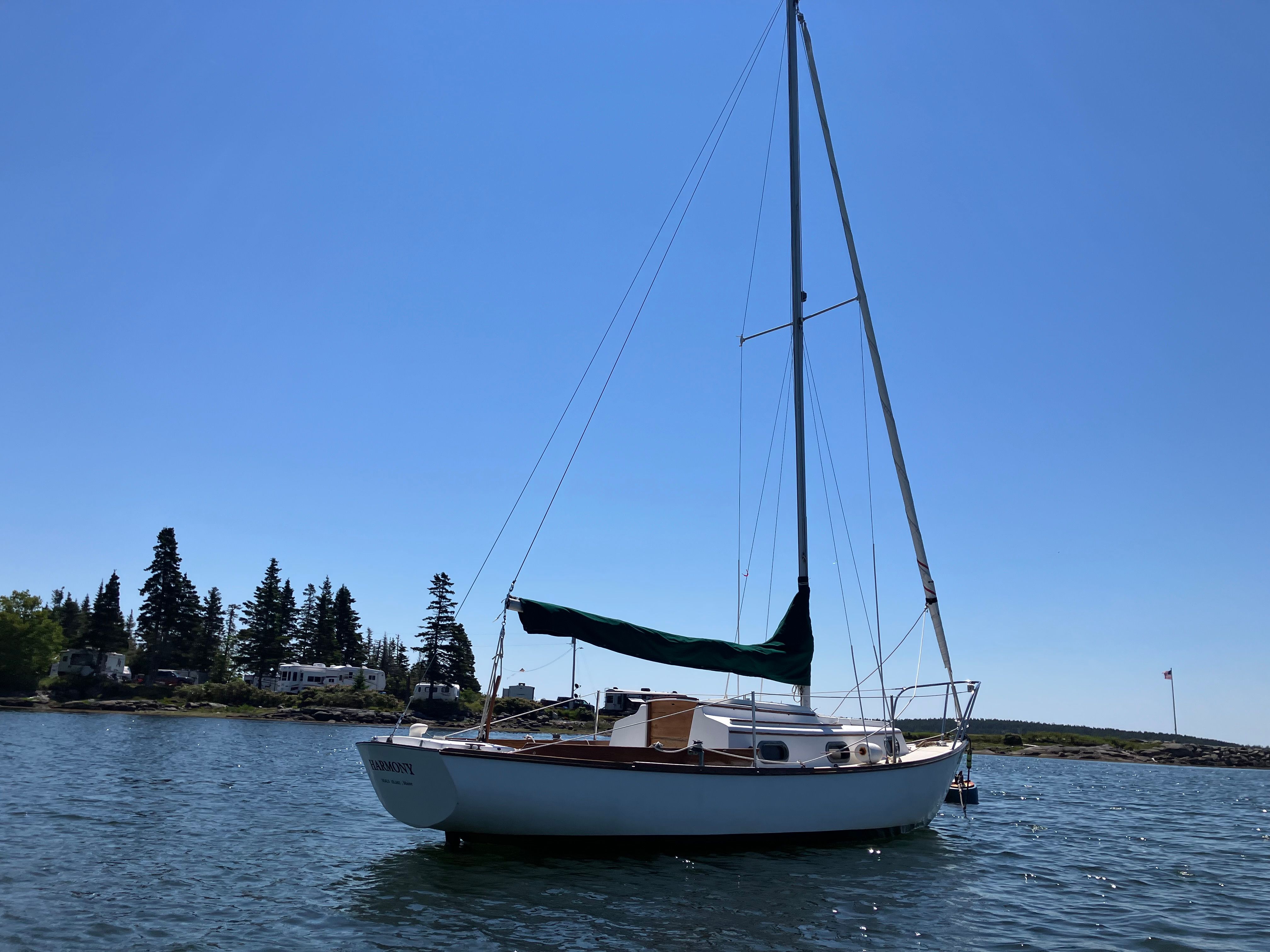A 1982 Cape Dory 25 sailboat rests calmly on the water, surrounded by trees.