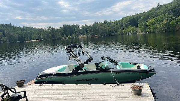 2022 MasterCraft NXT22 boat docked on a serene lake with forested background.
