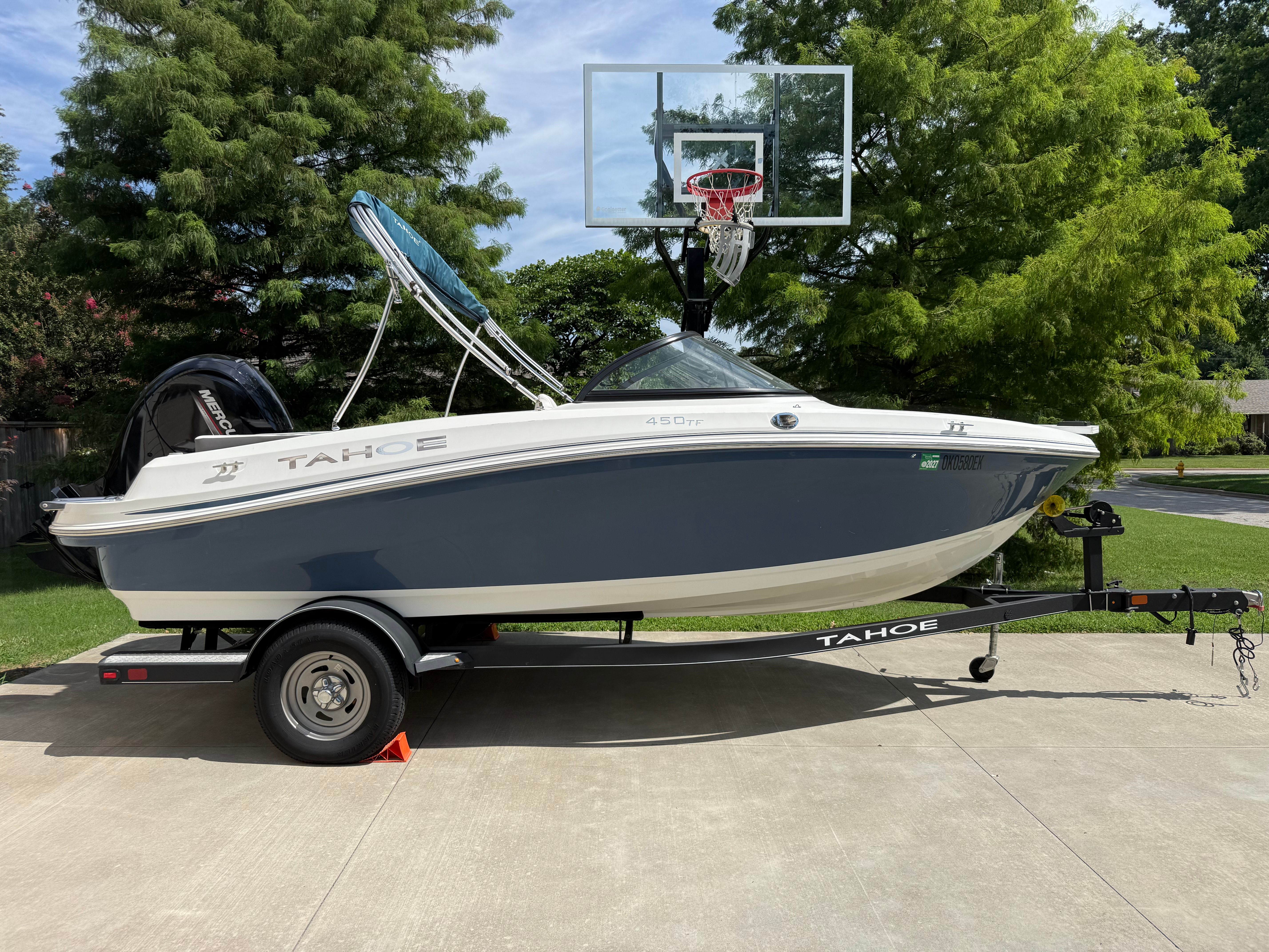 A 2019 Tahoe 450 TF boat on a trailer, parked on a driveway next to a basketball hoop.