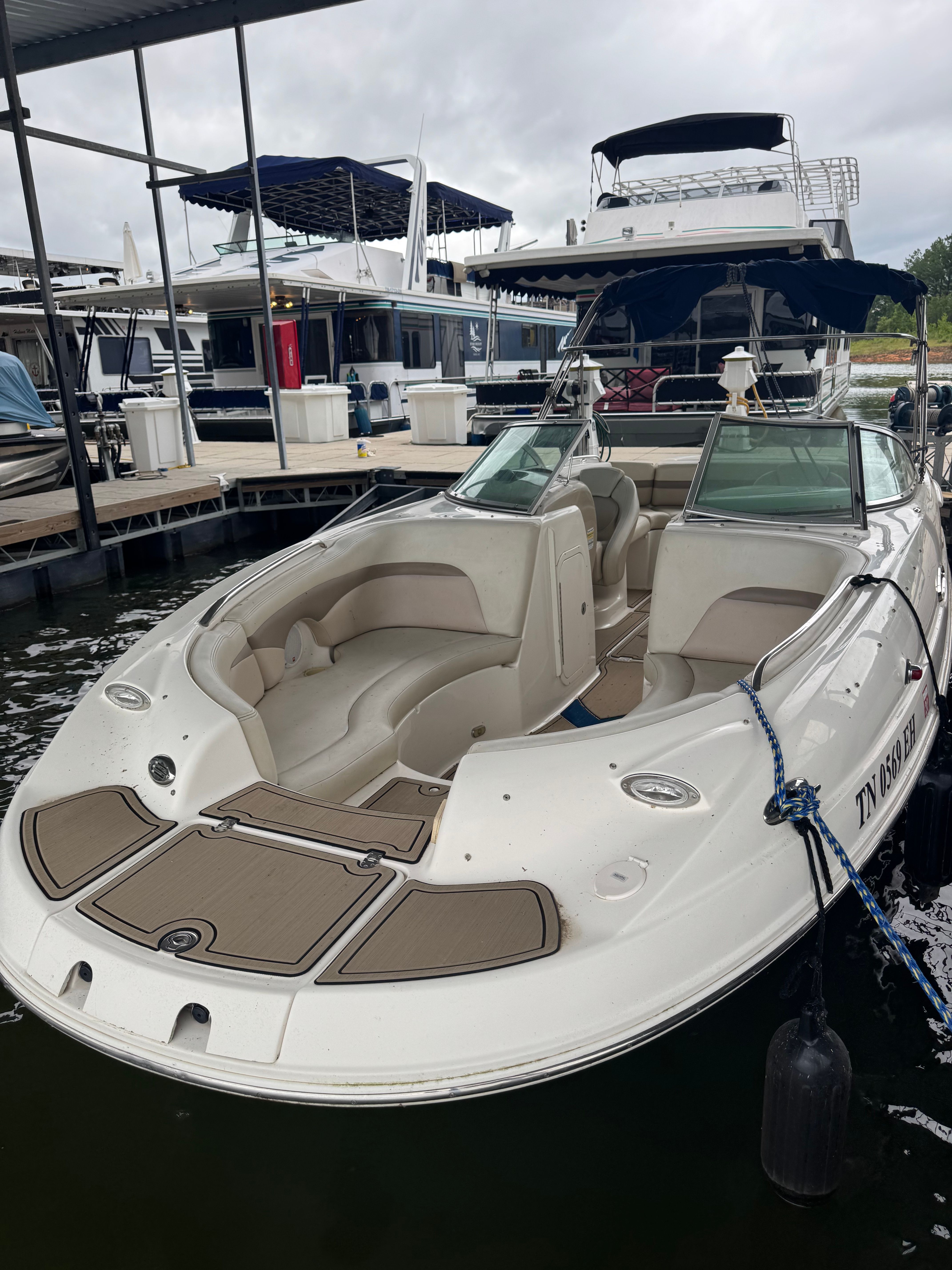 A white Chaparral Sunesta 223 boat docked. It features beige seating and is secured with ropes.