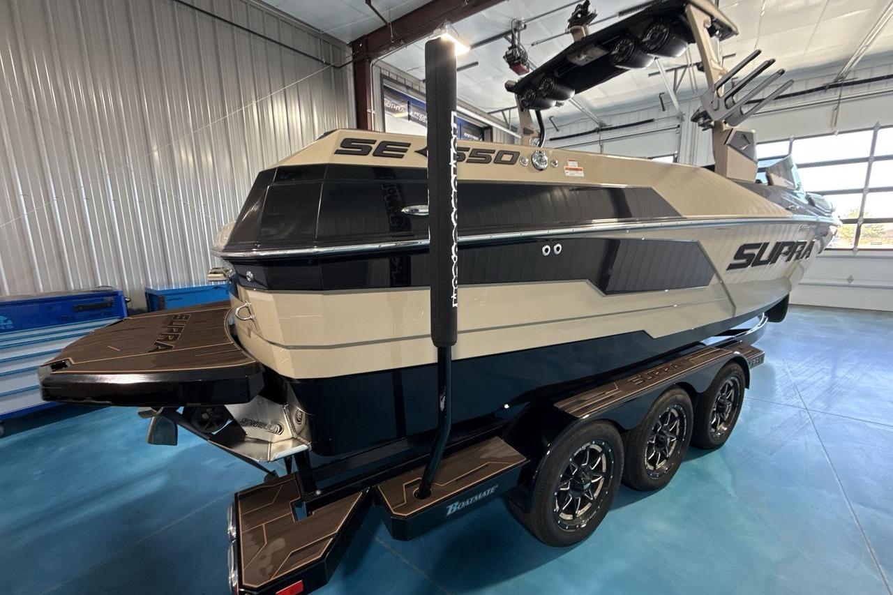 2023 Supra SE 550 boat in showroom, featuring sleek design and triple-axle trailer.