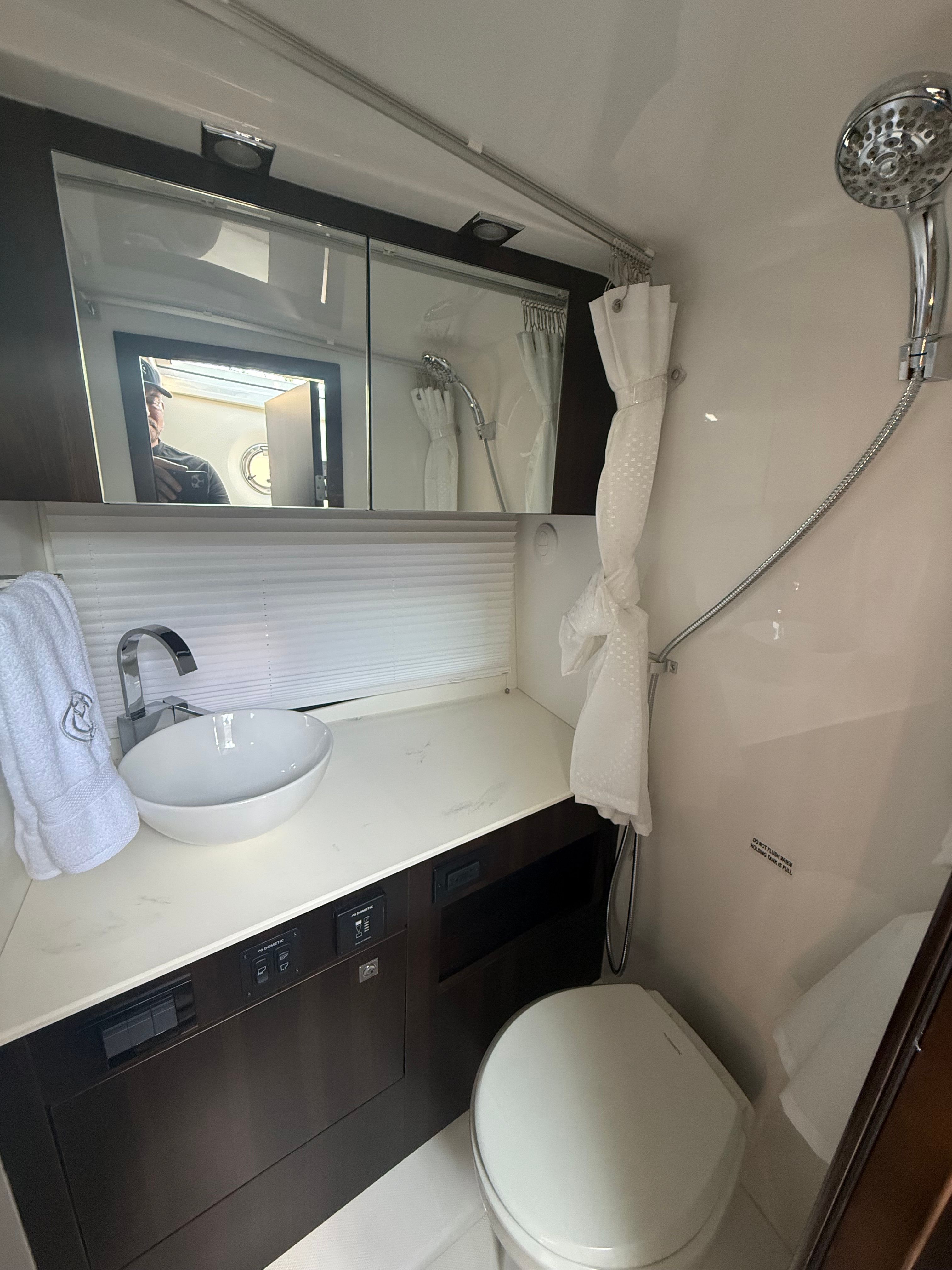 Yacht bathroom with sink, mirror, toilet, and shower. Sleek, modern design.