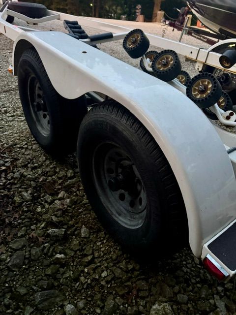 A boat trailer with two large wheels is on a gravel surface.