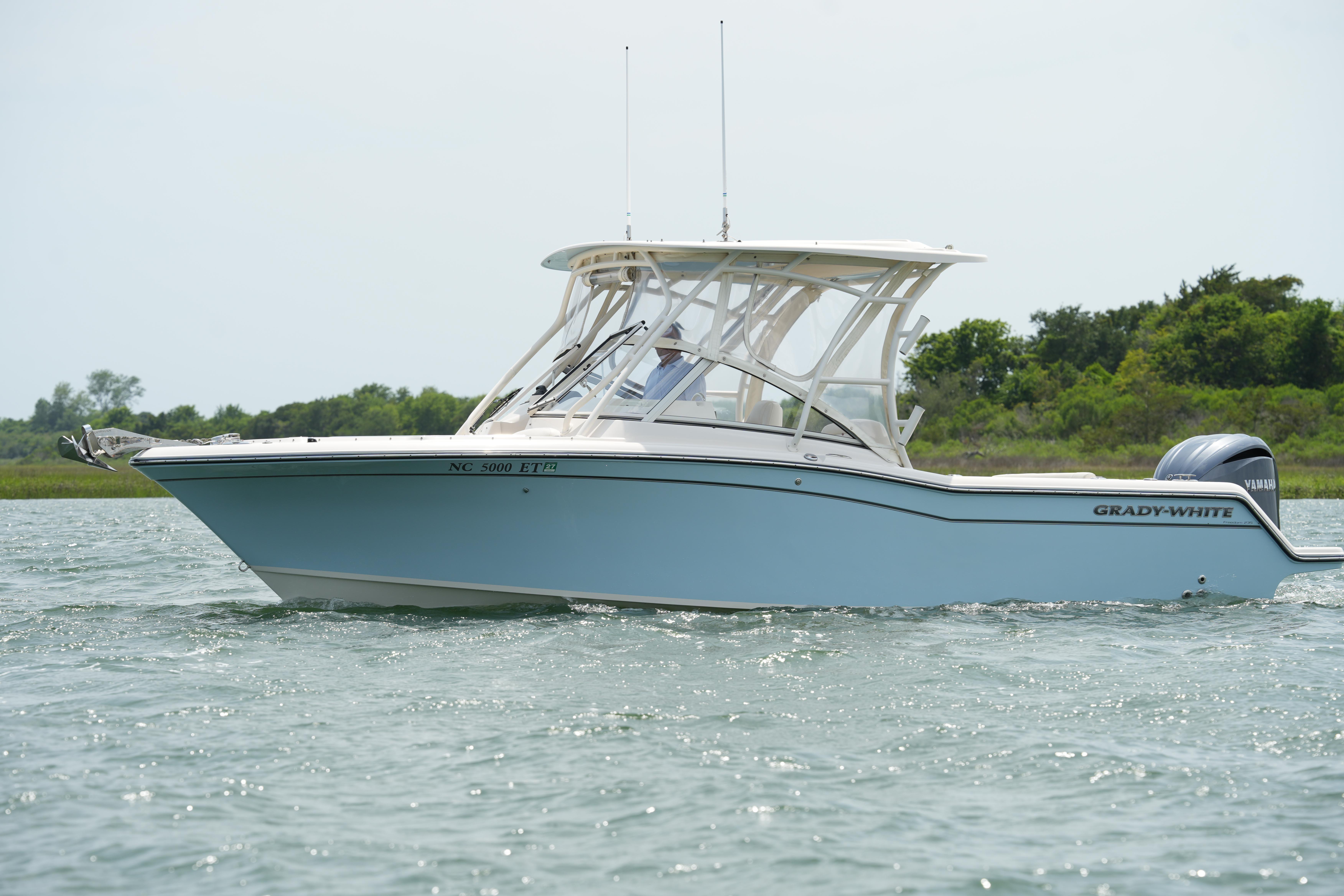 2021 Grady-White Freedom 235 boat cruising on water near lush shoreline.