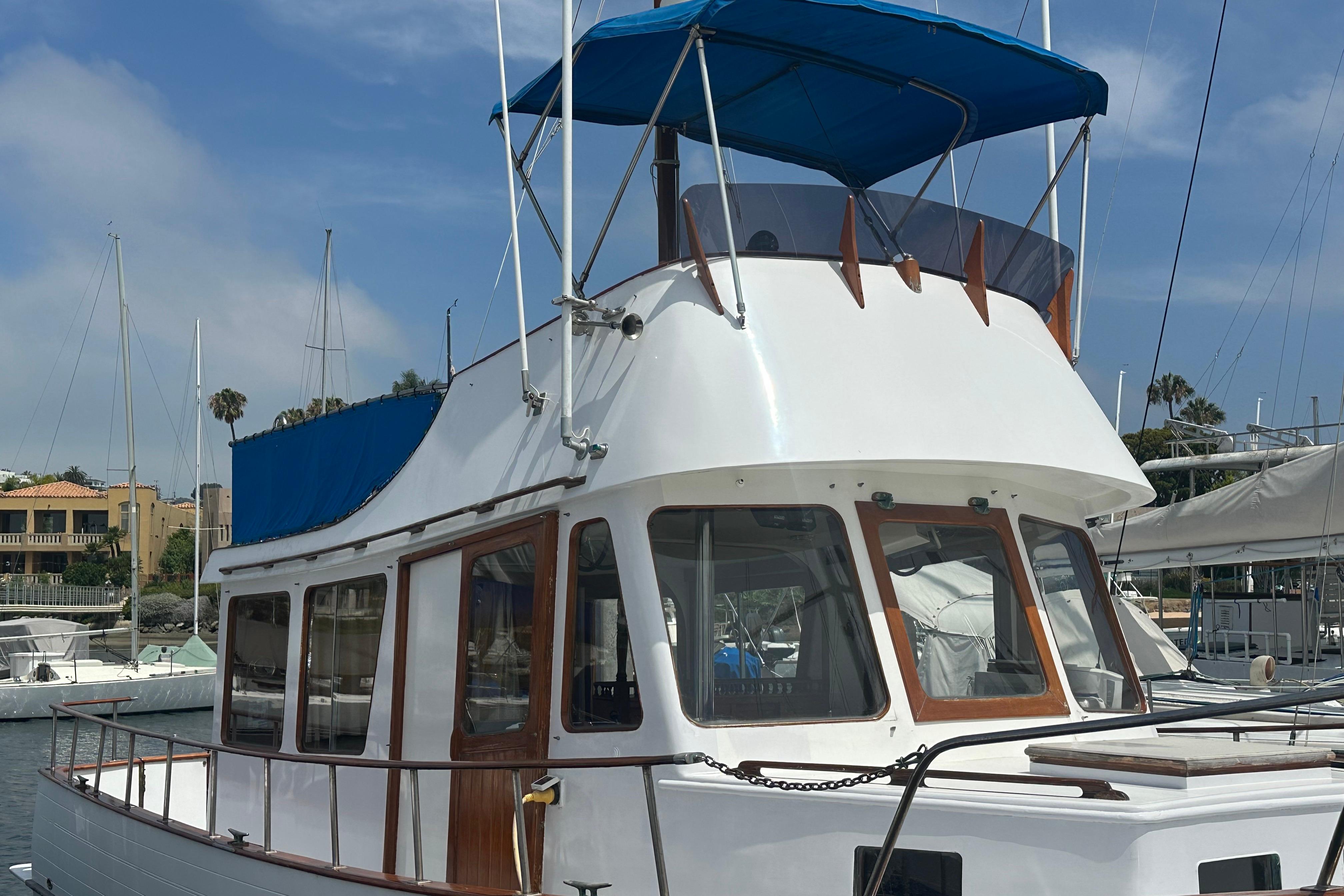 1973 CHB 33 boat with blue canopy docked at marina under clear sky.