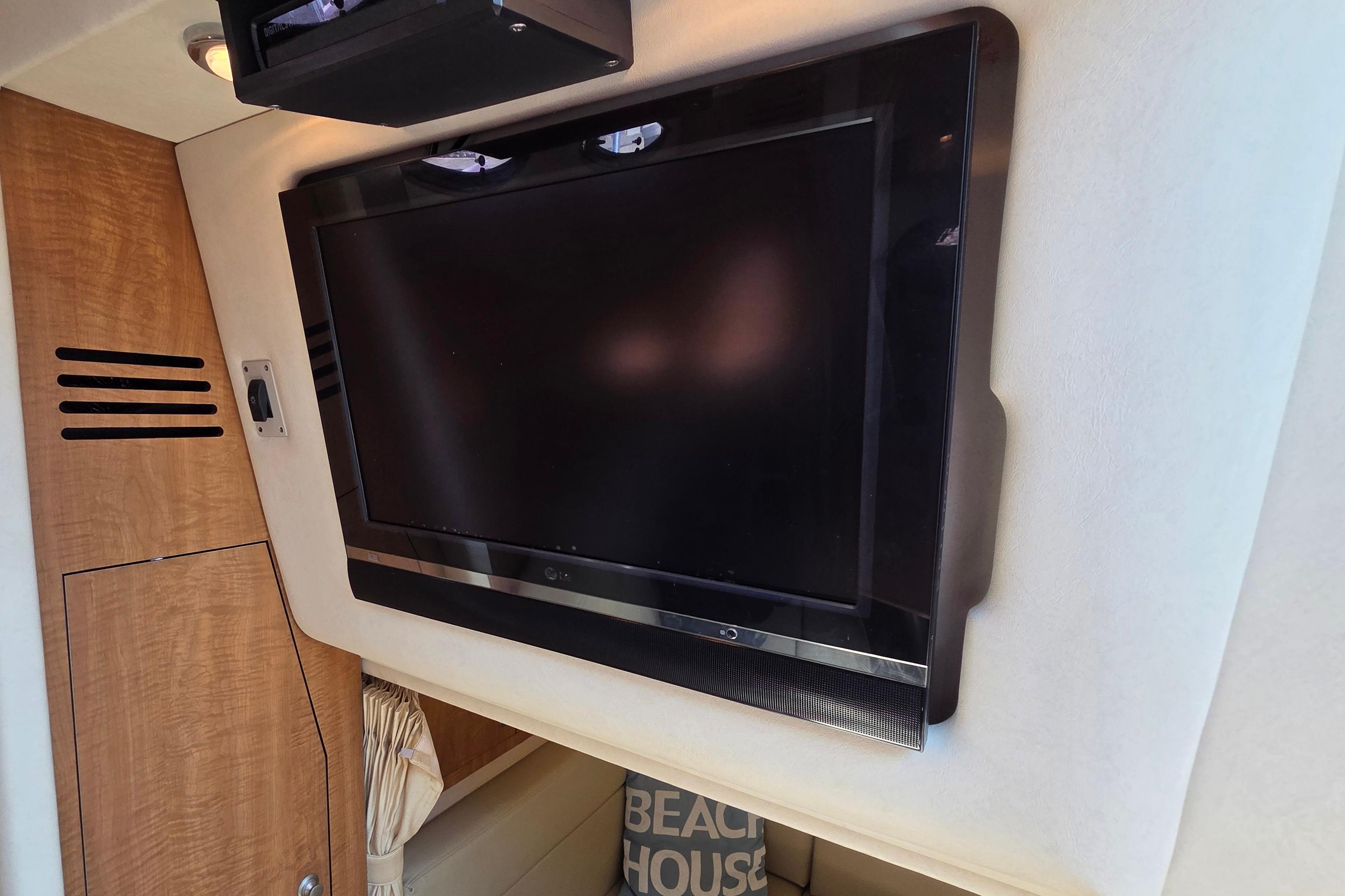 Flat-screen TV in 2006 Sea Ray Sundancer 320 cabin interior, featuring wood paneling and cozy decor.