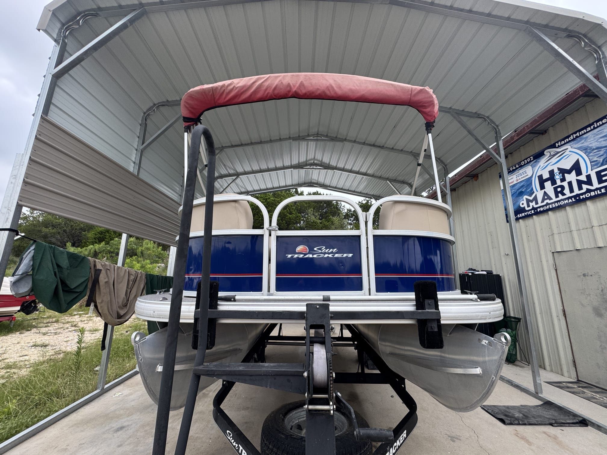 A 2018 Sun Tracker Party Barge 18 DLX on a trailer under a covered area.