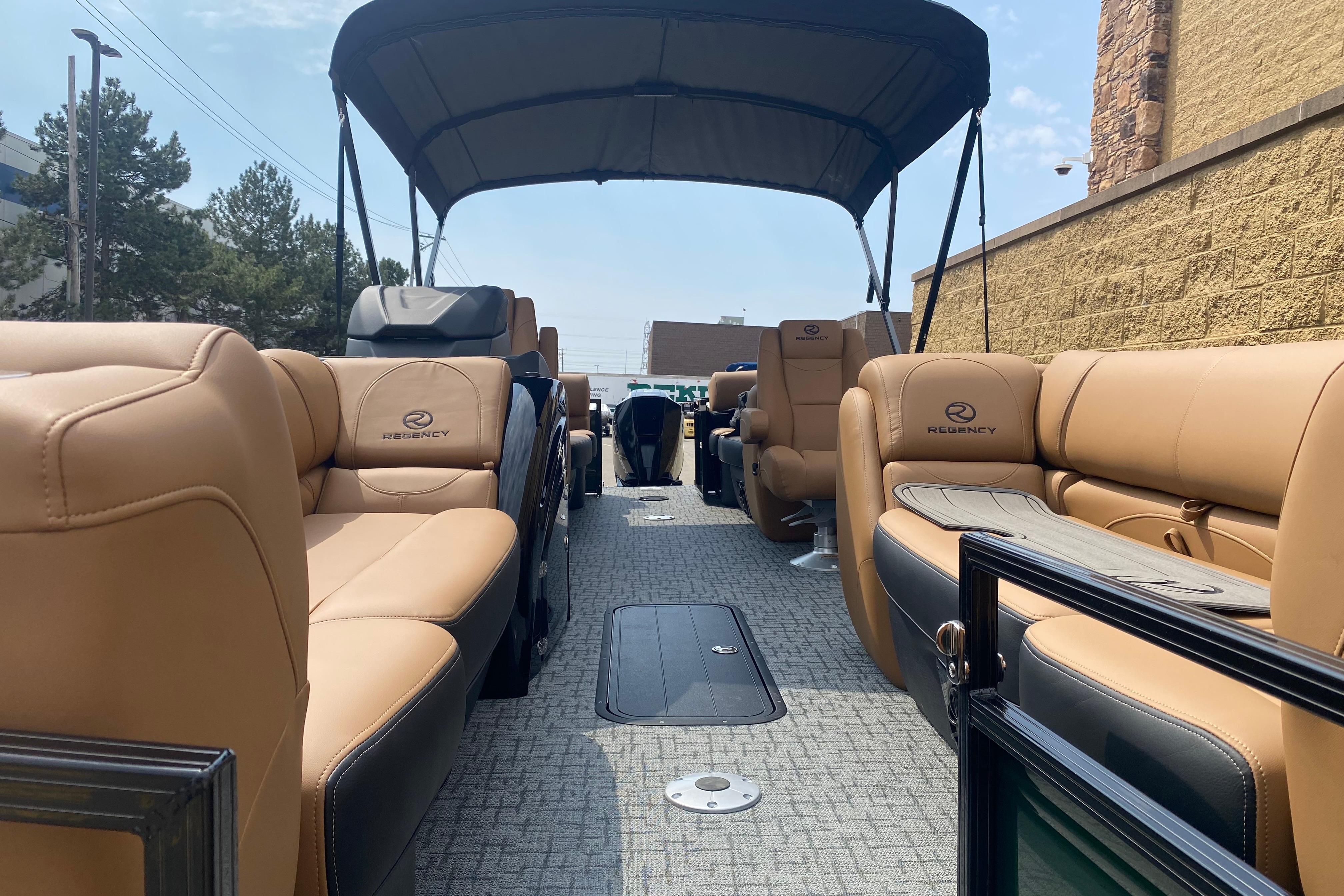 2026 Regency 230 DL pontoon boat with tan seating and canopy, parked outdoors.