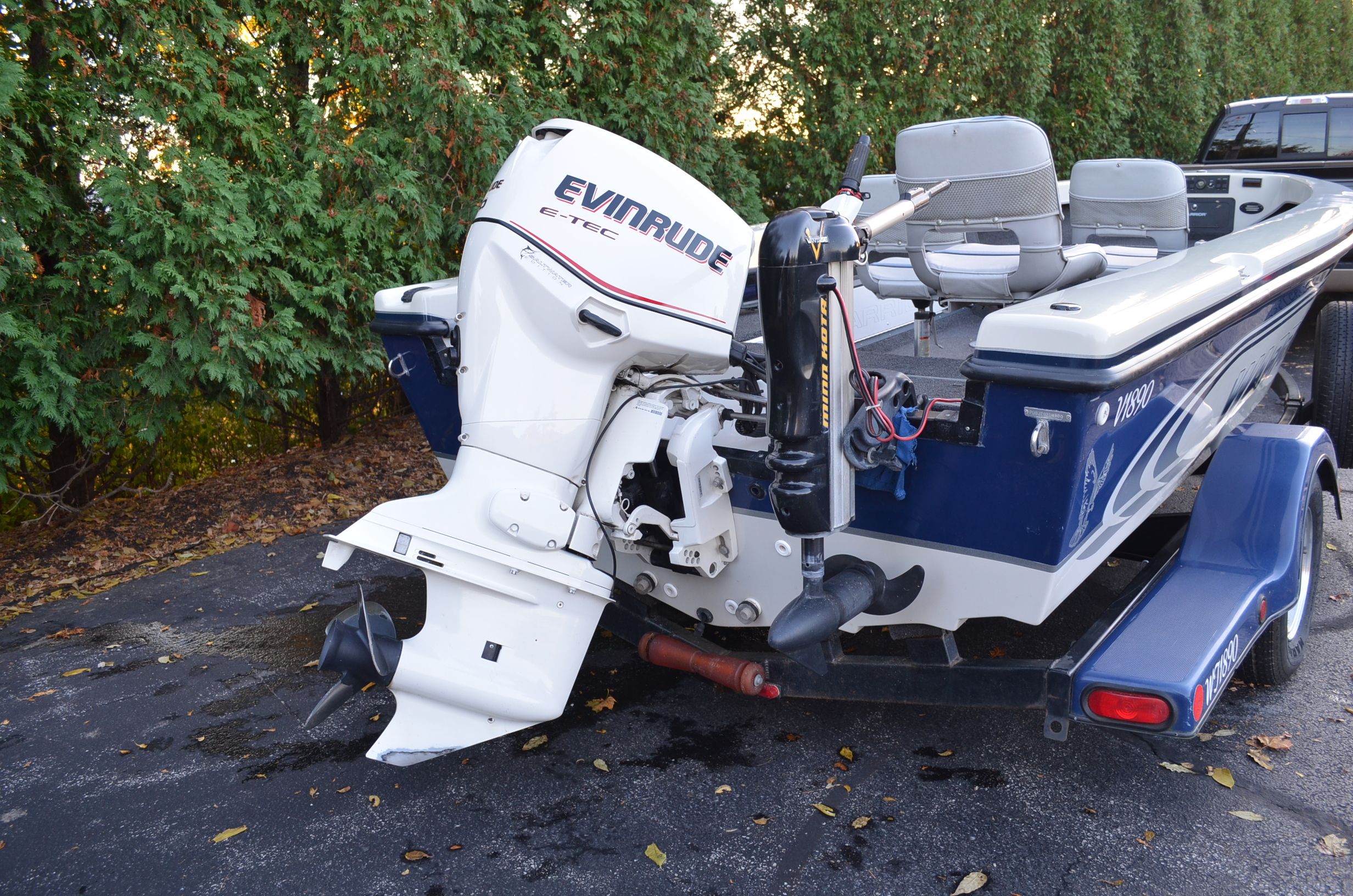 A blue and white boat with an Evinrude outboard motor on a trailer next to trees.