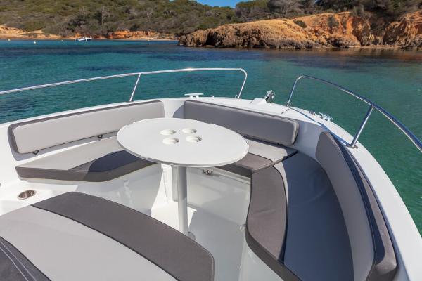 2023 Jeanneau Leader 6.5 CC S3 boat with seating area and table, anchored in clear waters.