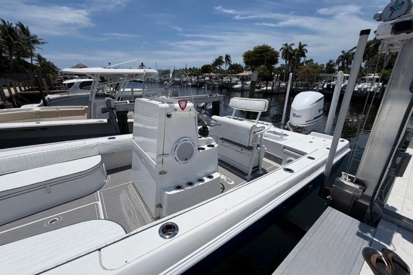 A white boat is docked in a sunny harbor with palm trees in the background.