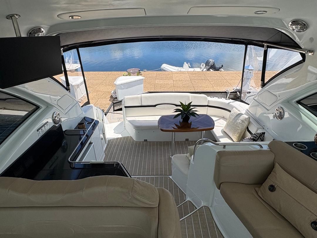 Interior of a luxury yacht with beige seating, a wooden table, and a view of the water.