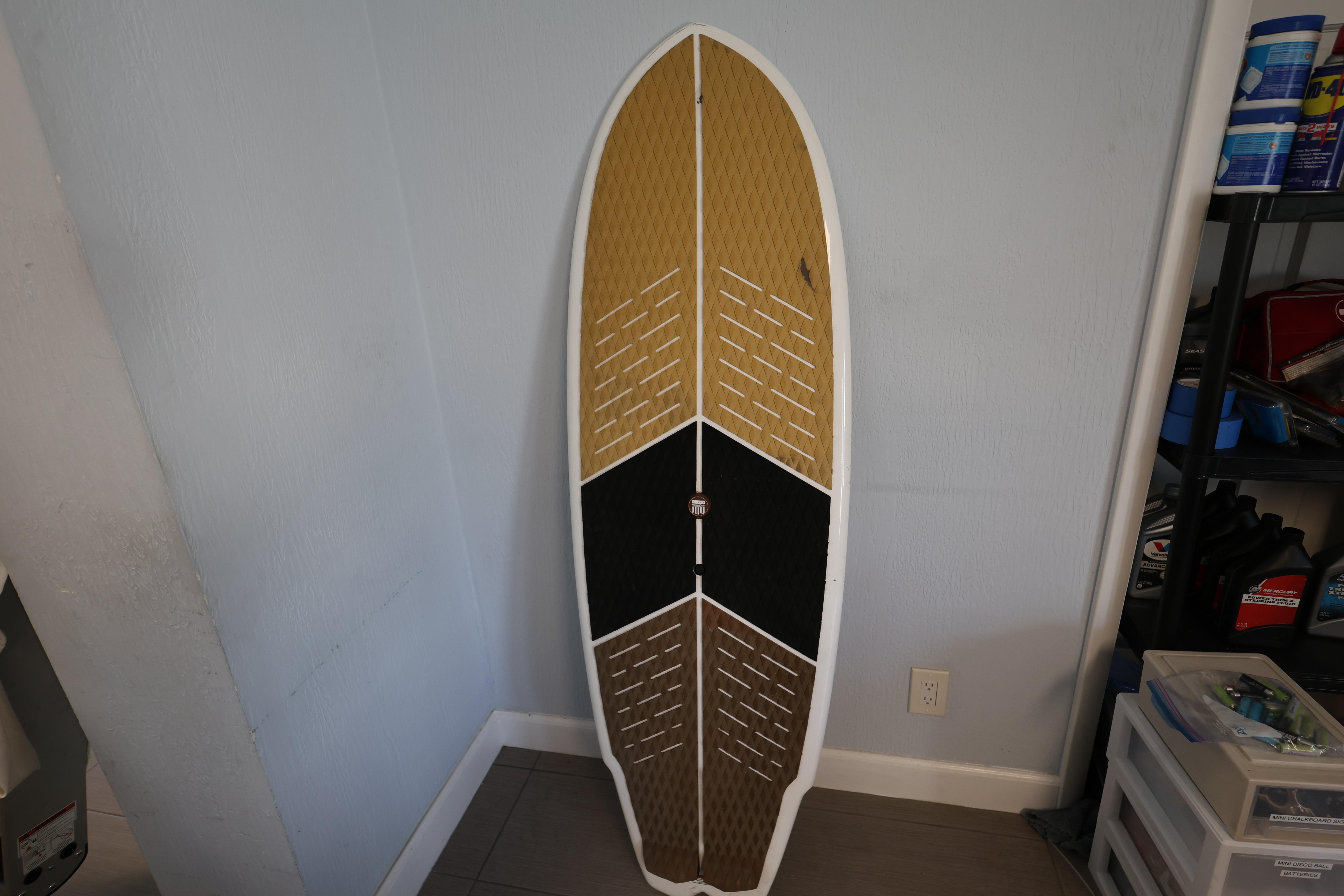 2023 MasterCraft X24 surfboard with a tri-color design, leaning against a wall indoors.
