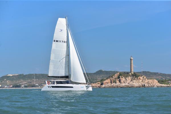 2025 Seawind 1170 sailing near a rocky coastline with a lighthouse.