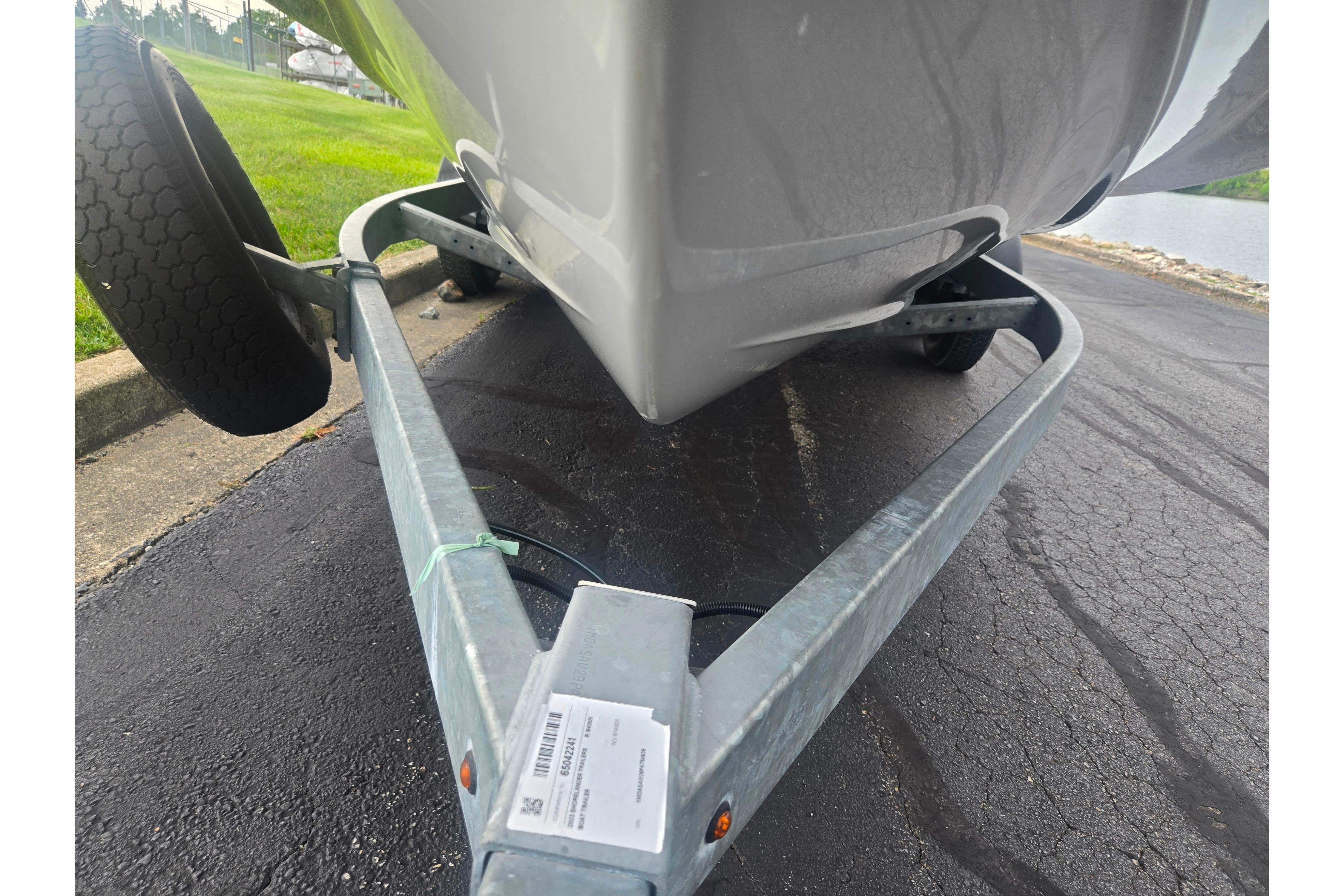 Trailer carrying 2023 Yamaha Boats 252S, parked on asphalt near water.