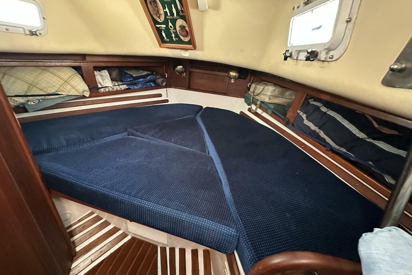 Cozy cabin interior of 1979 Hughes 3910 sailboat with blue cushions and wooden accents.