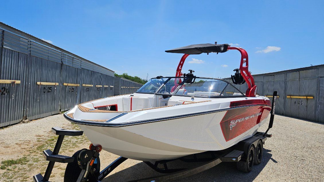 A white and red sport boat on a trailer in a fenced area.