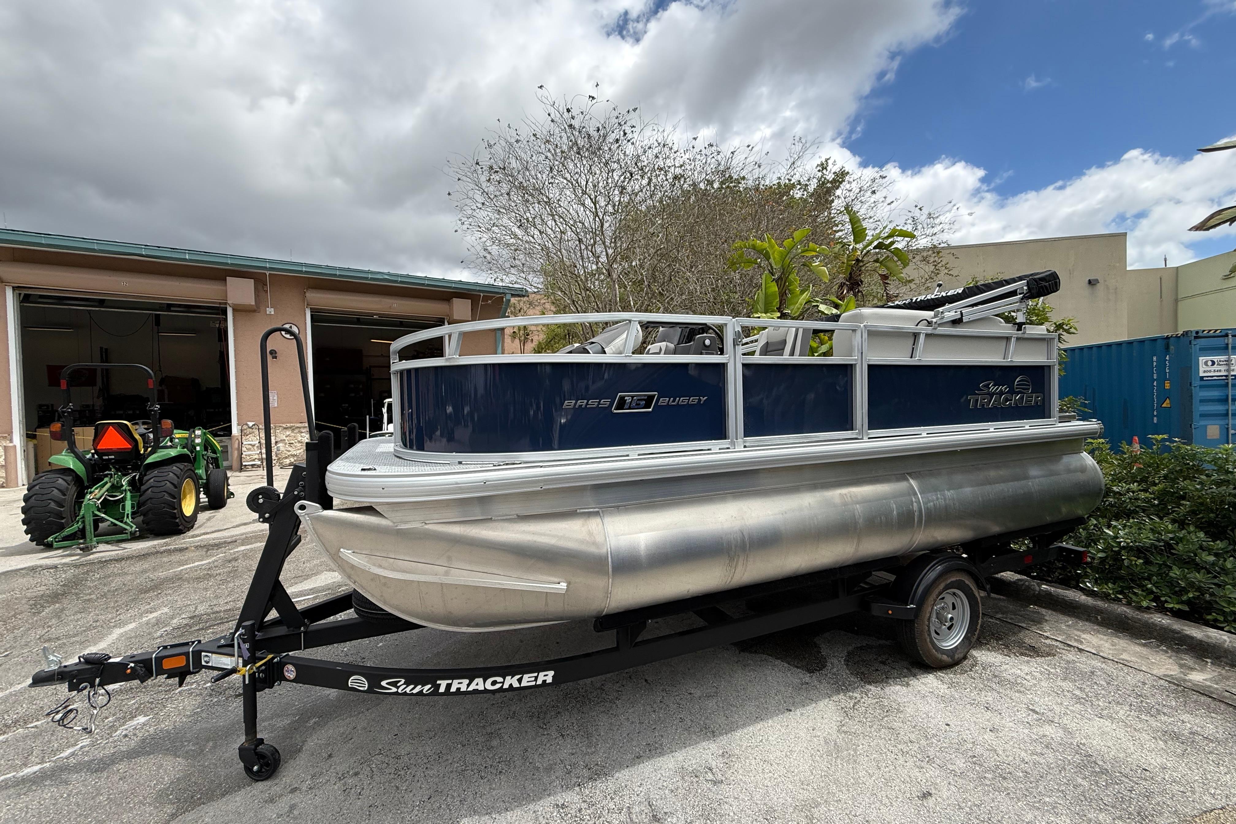 2026 Sun Tracker Bass Buggy 16 XL Select pontoon boat on trailer, parked outdoors.