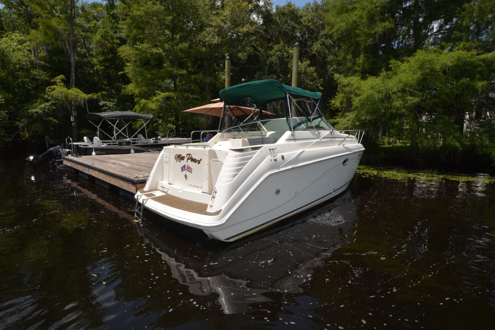 1999 Rinker 270 Fiesta Vee boat docked on a serene lake with lush greenery.