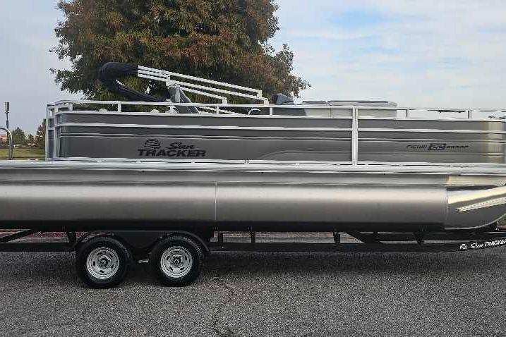 2026 Sun Tracker Fishin' Barge 22 DLX pontoon boat on trailer, parked outdoors.