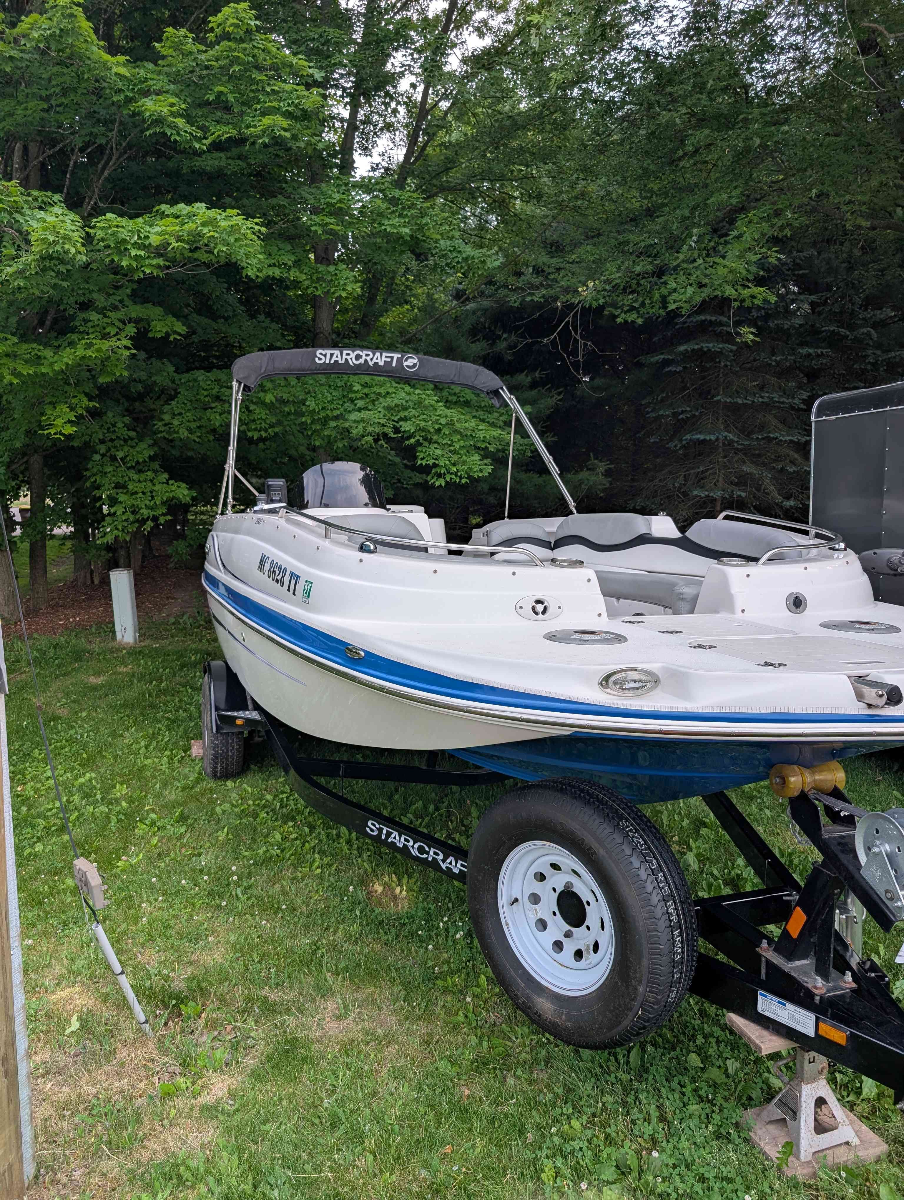 2015 Starcraft 2000 boat on trailer in a green setting.