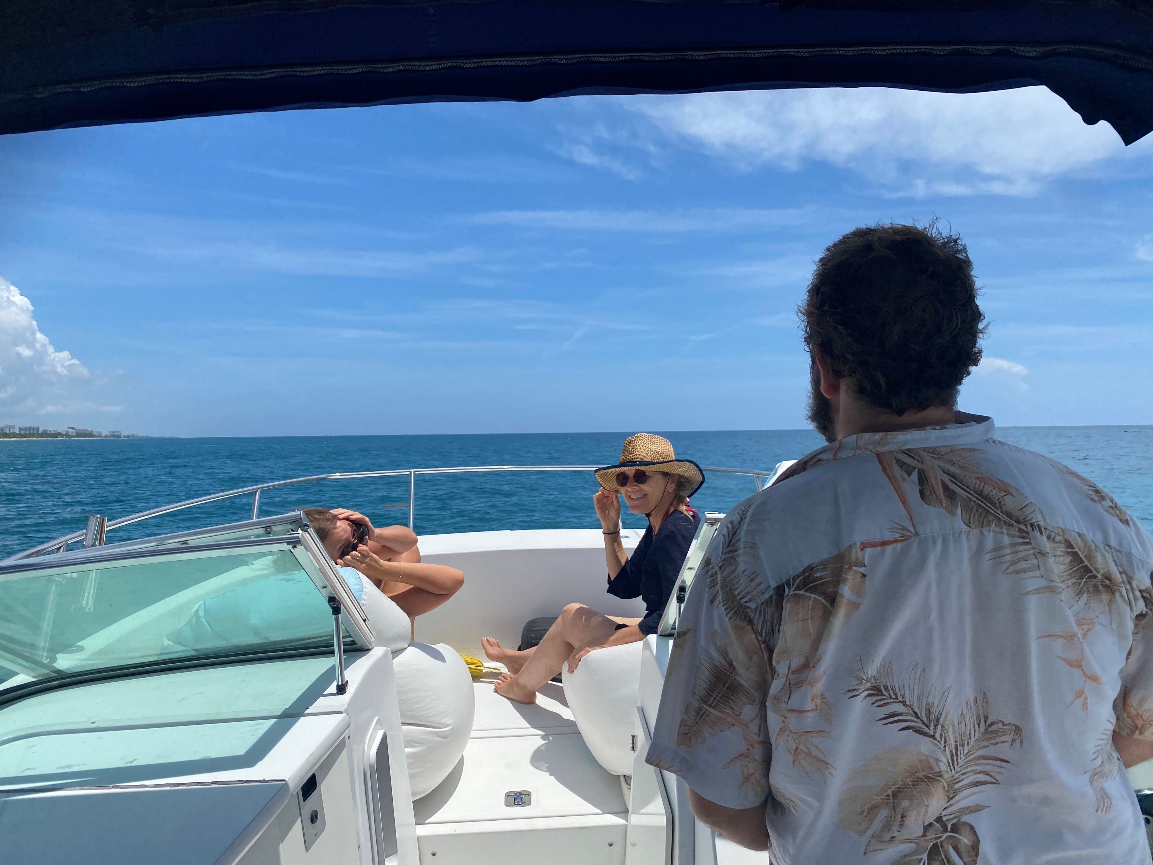 Three people relaxing on a boat at sea under a blue sky.