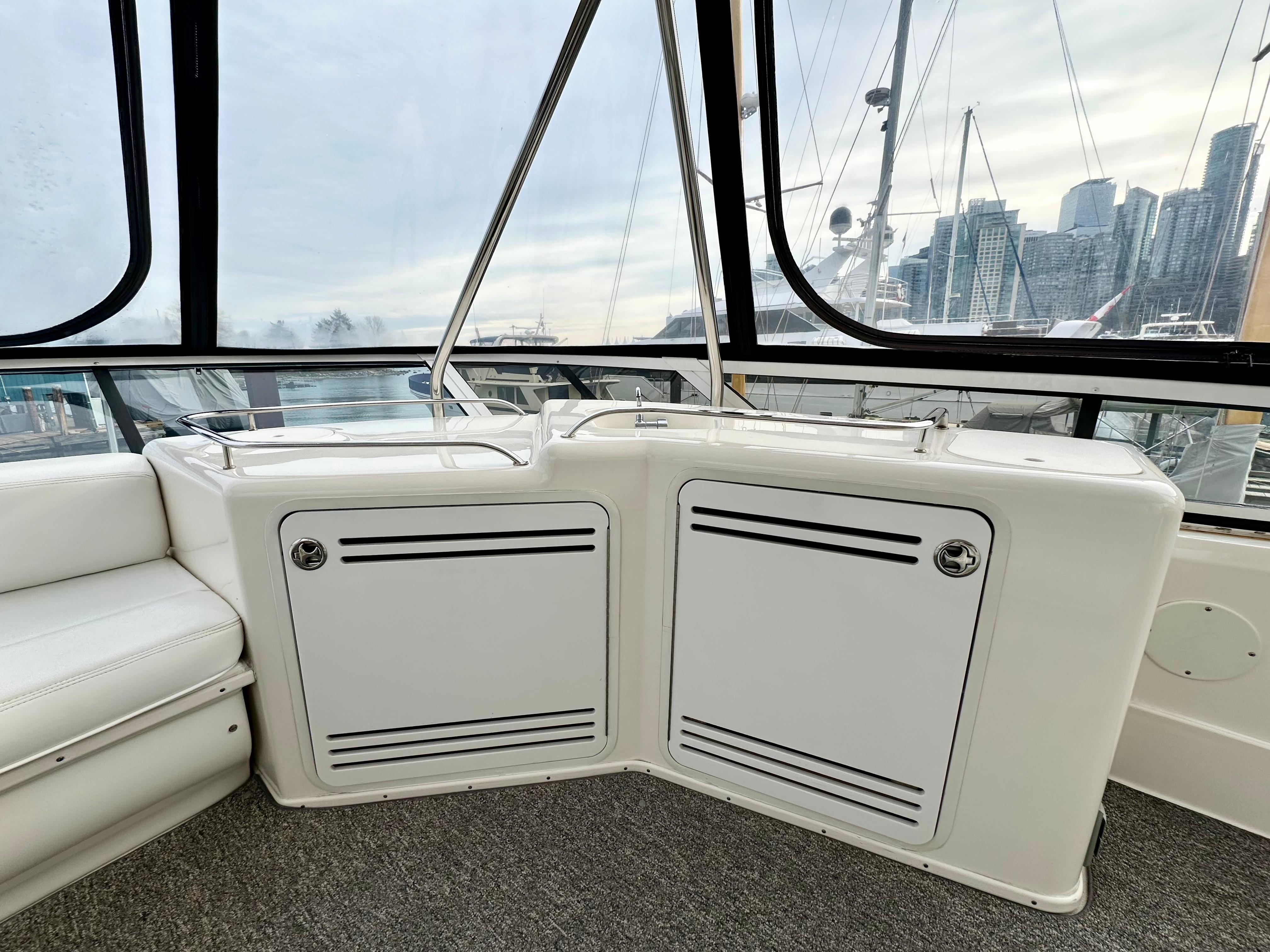 2002 Sea Ray 560 Sedan Bridge interior with white seating and storage, overlooking marina skyline.