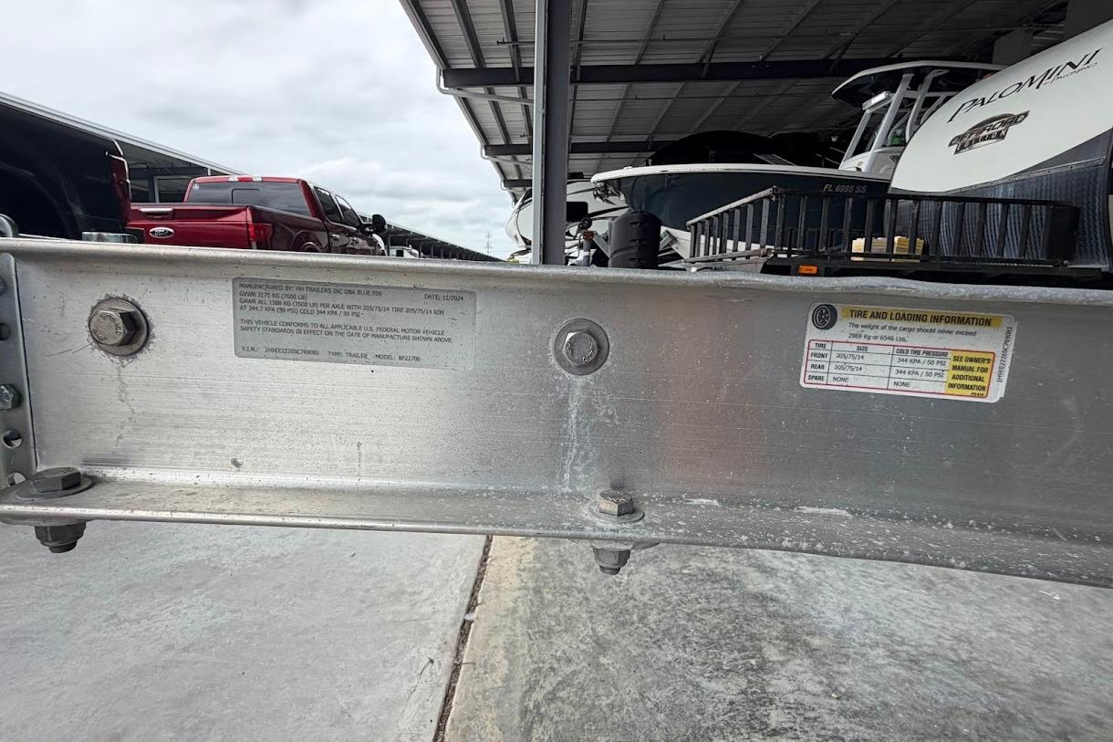 Boat trailer with tire and loading information, parked under a shelter with vehicles nearby.