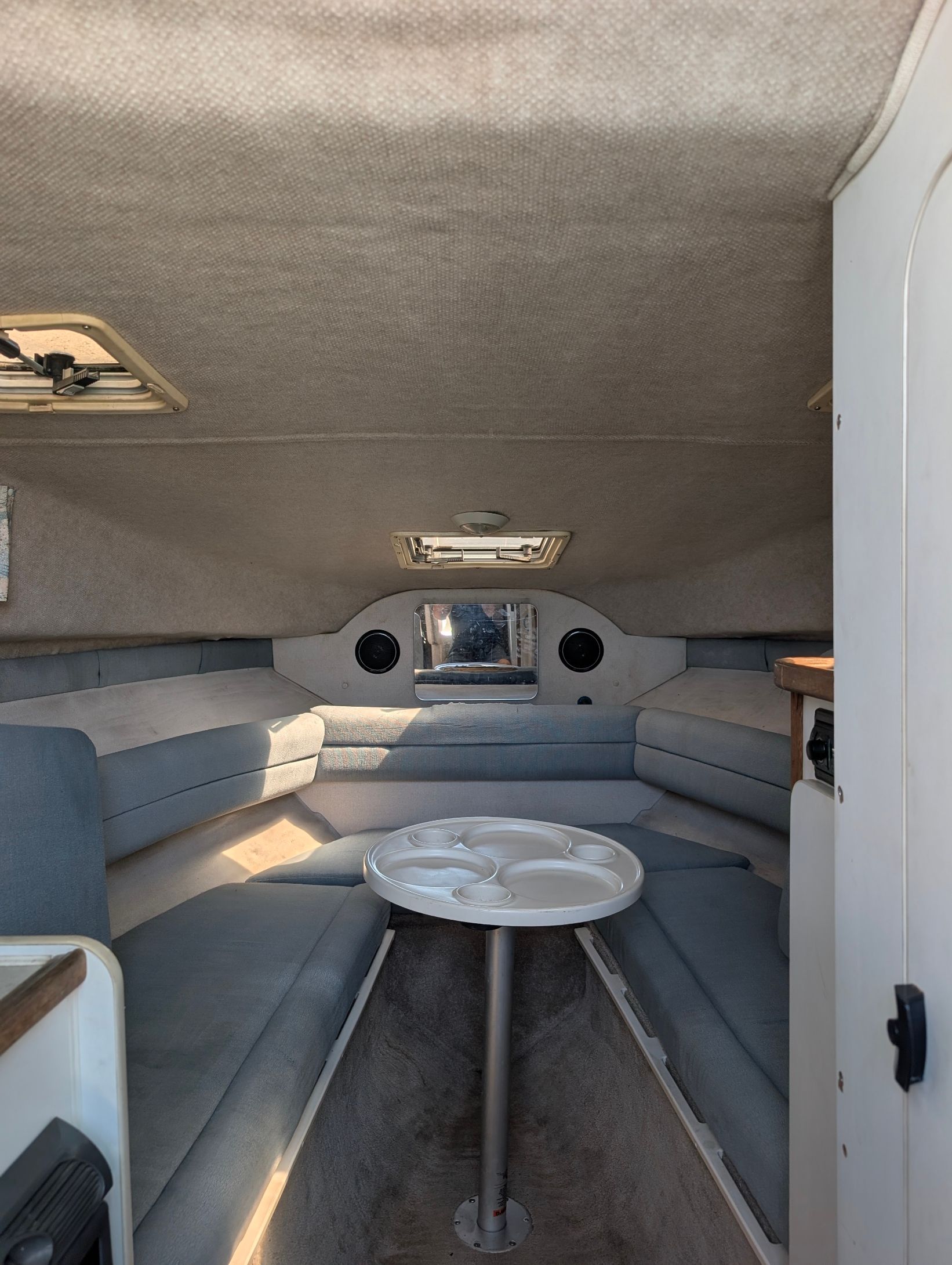 Interior of the 1995 Rinker Fiesta Vee 265 with gray upholstery and a round table.