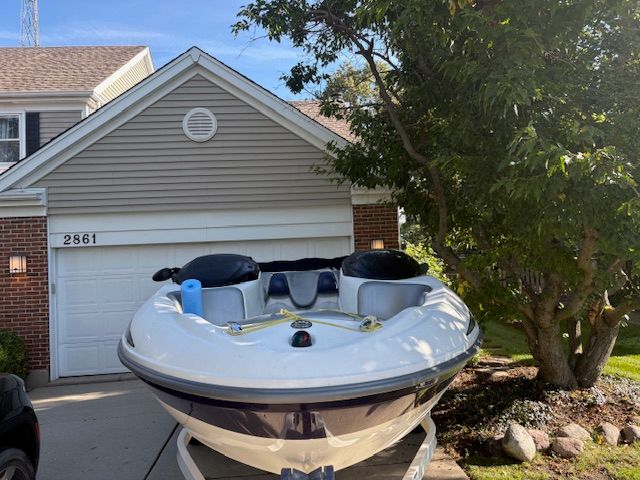2004 Bombardier Challenger boat parked in driveway near garage and tree.