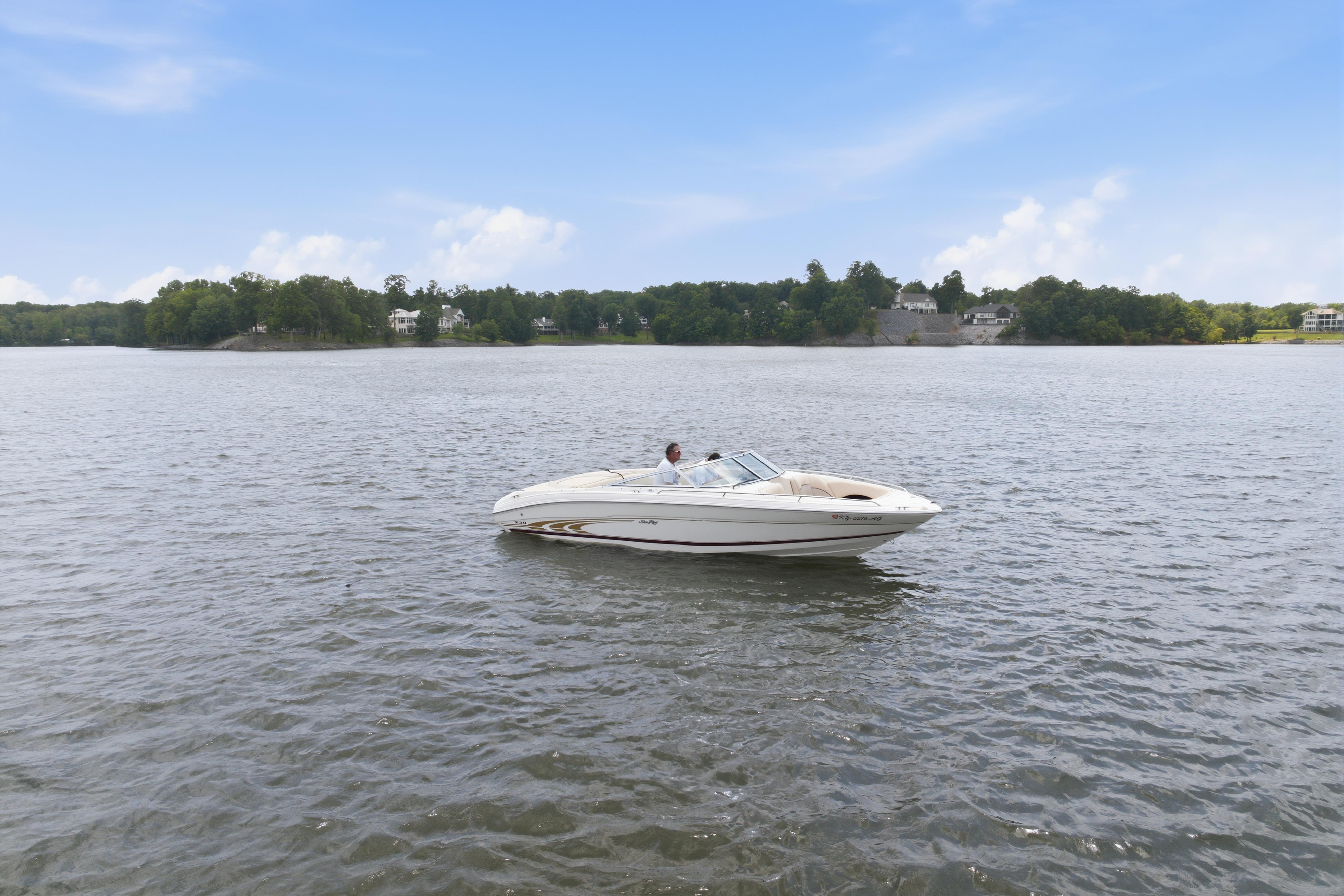 1997 Sea Ray 230 Signature boat cruising on a serene lake under a clear blue sky.