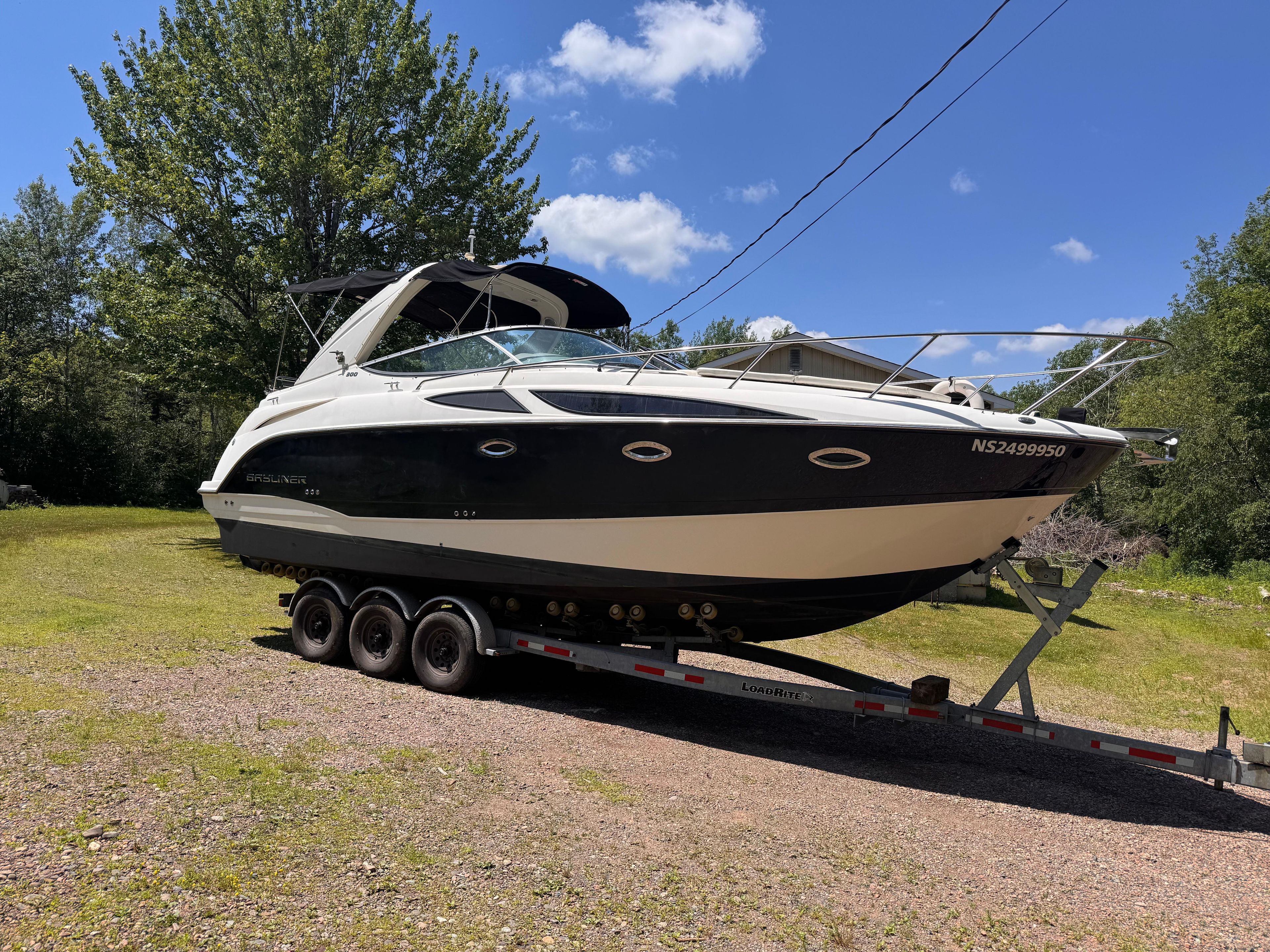 2009 Bayliner 300 boat on trailer, parked on grassy area under clear blue sky.