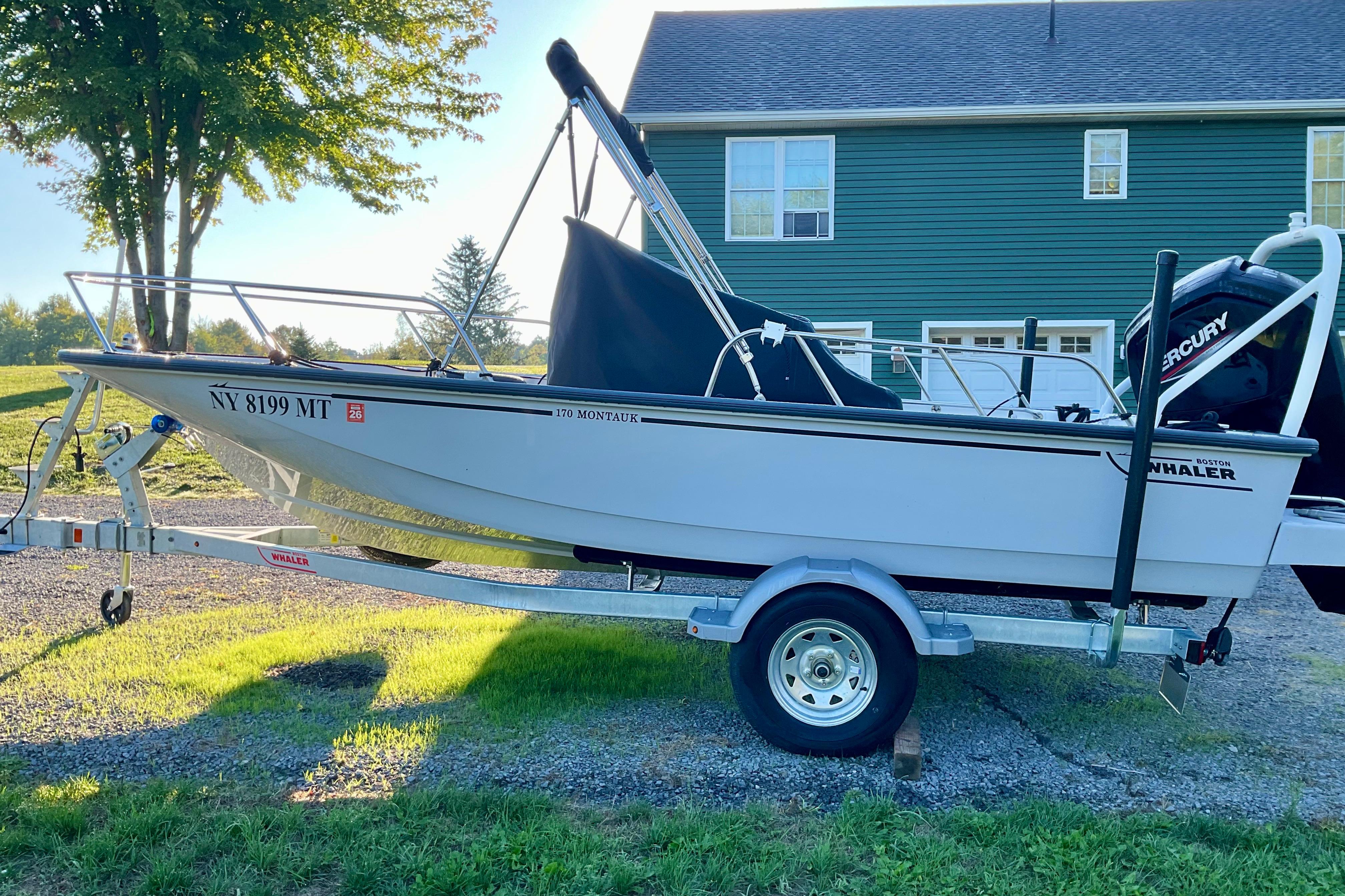 2024 Boston Whaler 170 Montauk boat on trailer, parked in front of a green house.