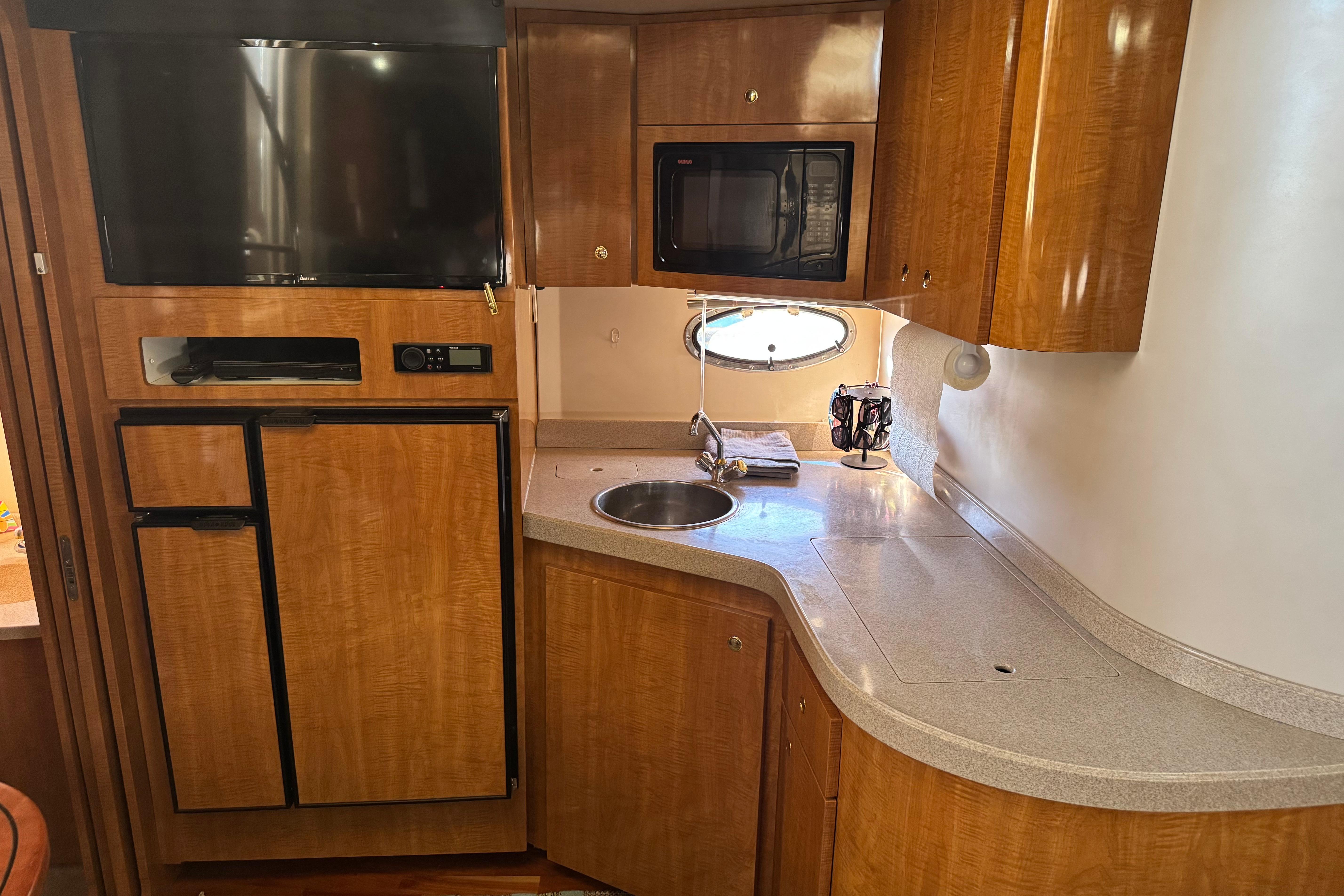2007 Regal Commodore 3860 yacht kitchen with wood cabinetry, sink, microwave, and TV.