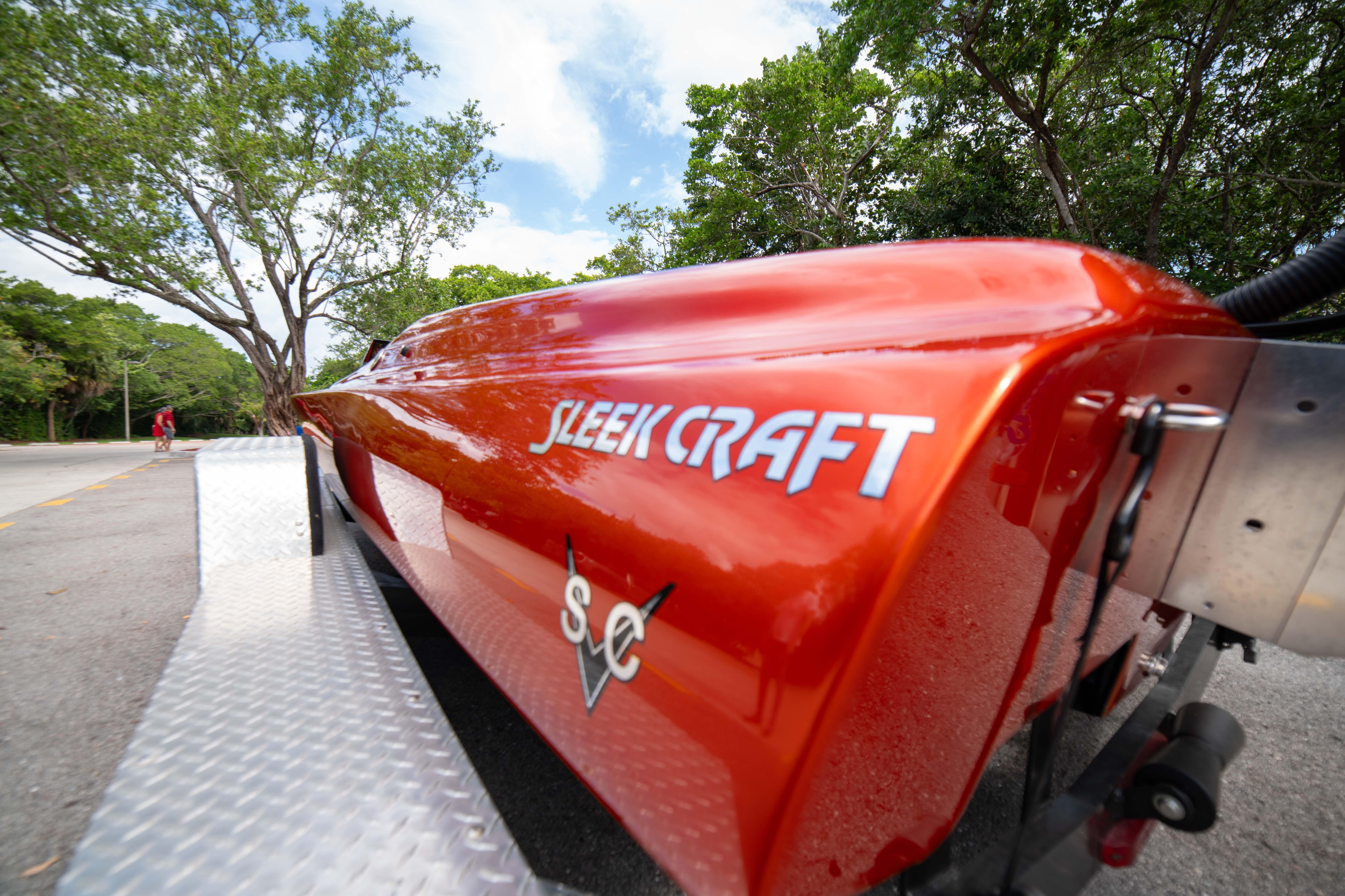 1984 Sleekcraft Aristocrat 20 boat on trailer, vibrant orange finish, parked near trees.