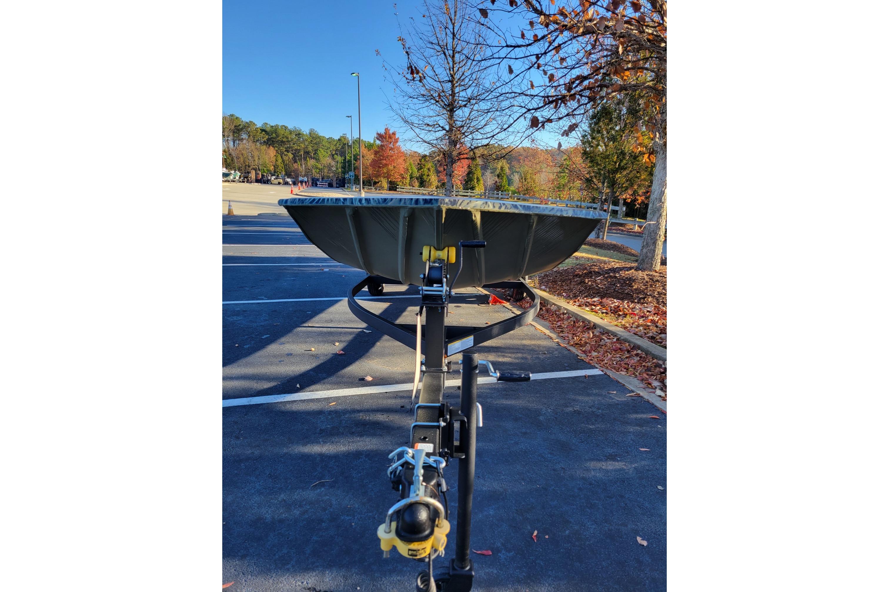 2025 Tracker Grizzly 1860 Utility boat on trailer in parking lot, autumn trees in background.
