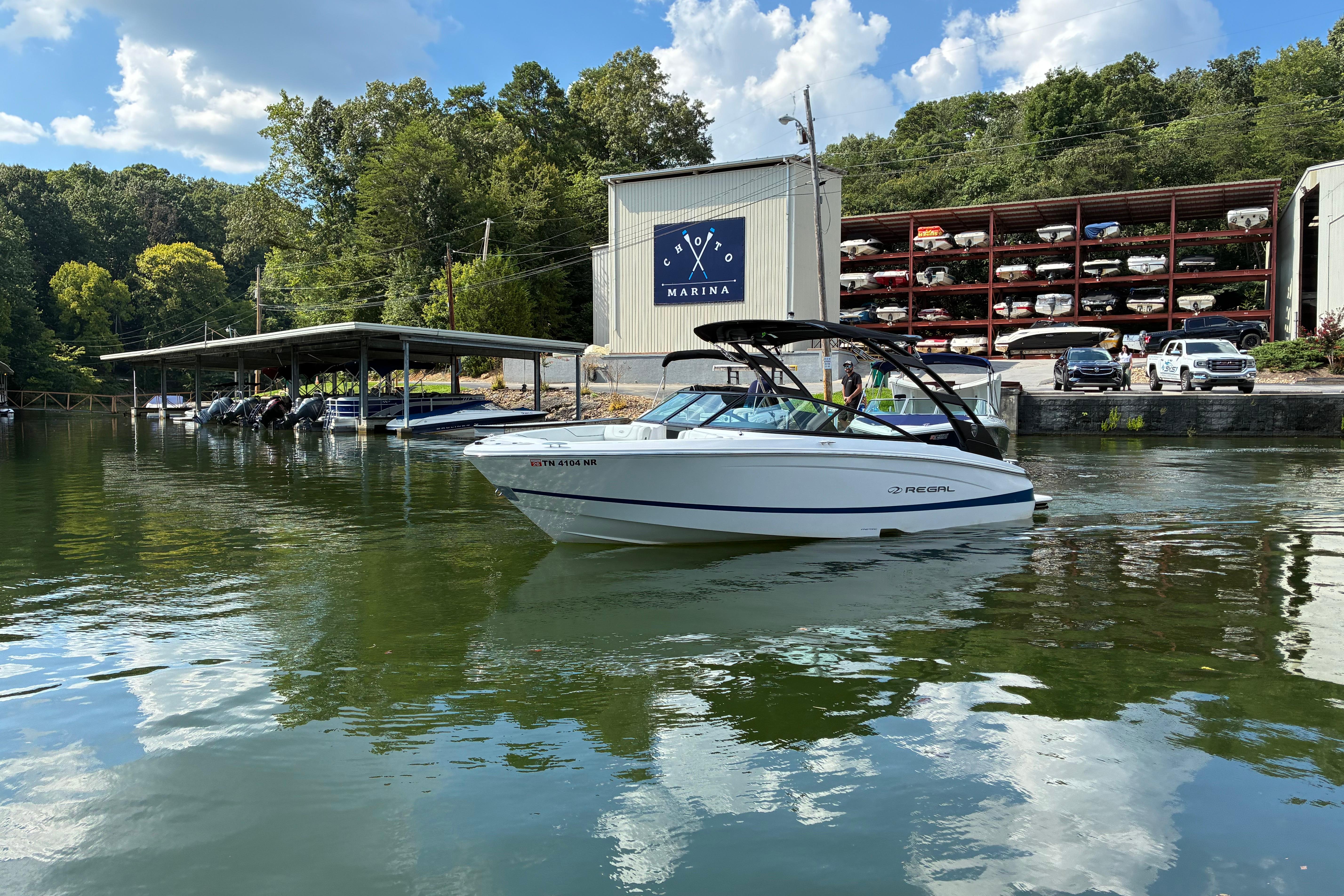 2025 Regal LS2 boat cruising near a marina with docked boats and lush greenery.