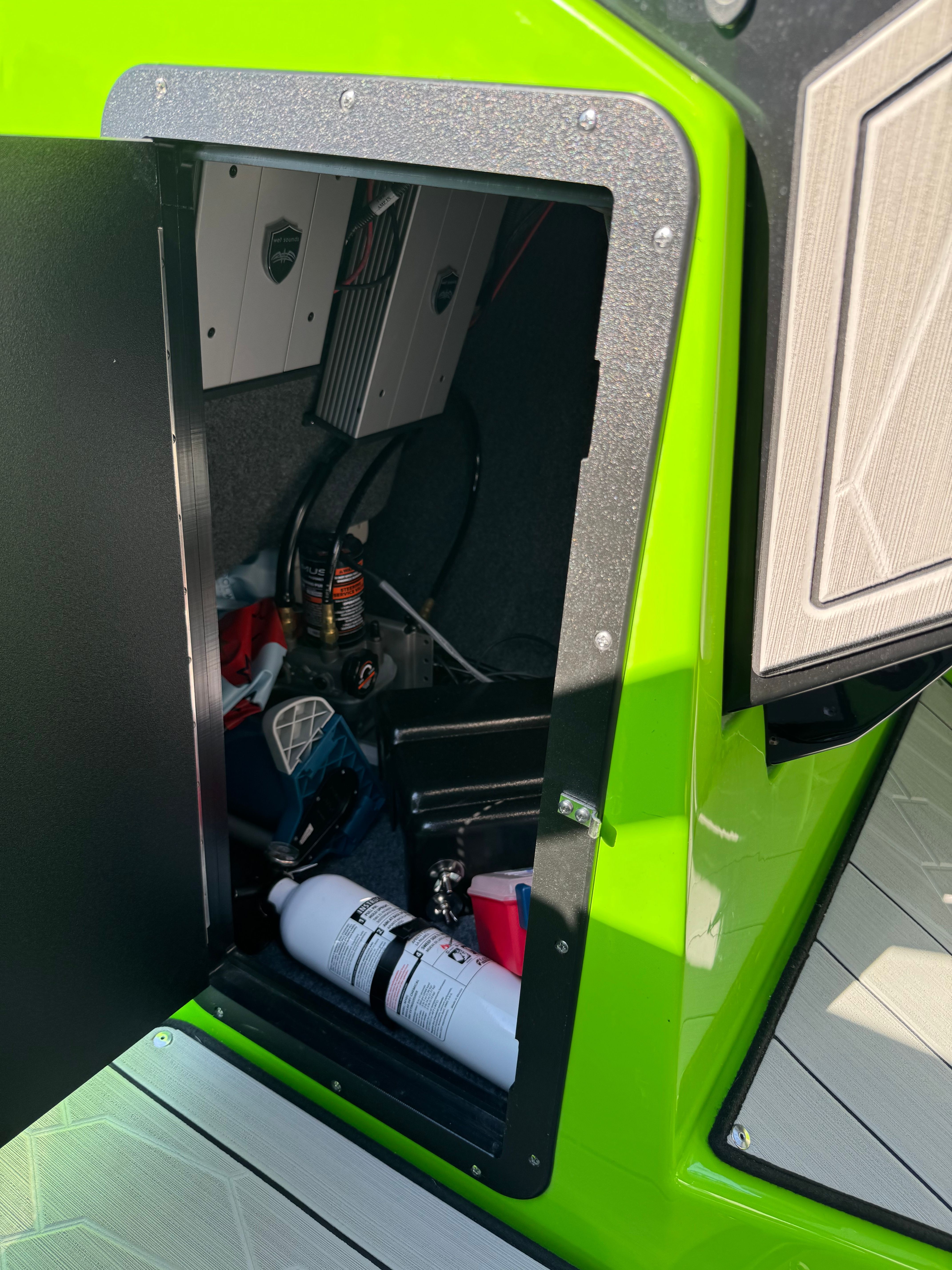 An open storage compartment on a green Yamaha 255XD boat shows equipment and a fire extinguisher.