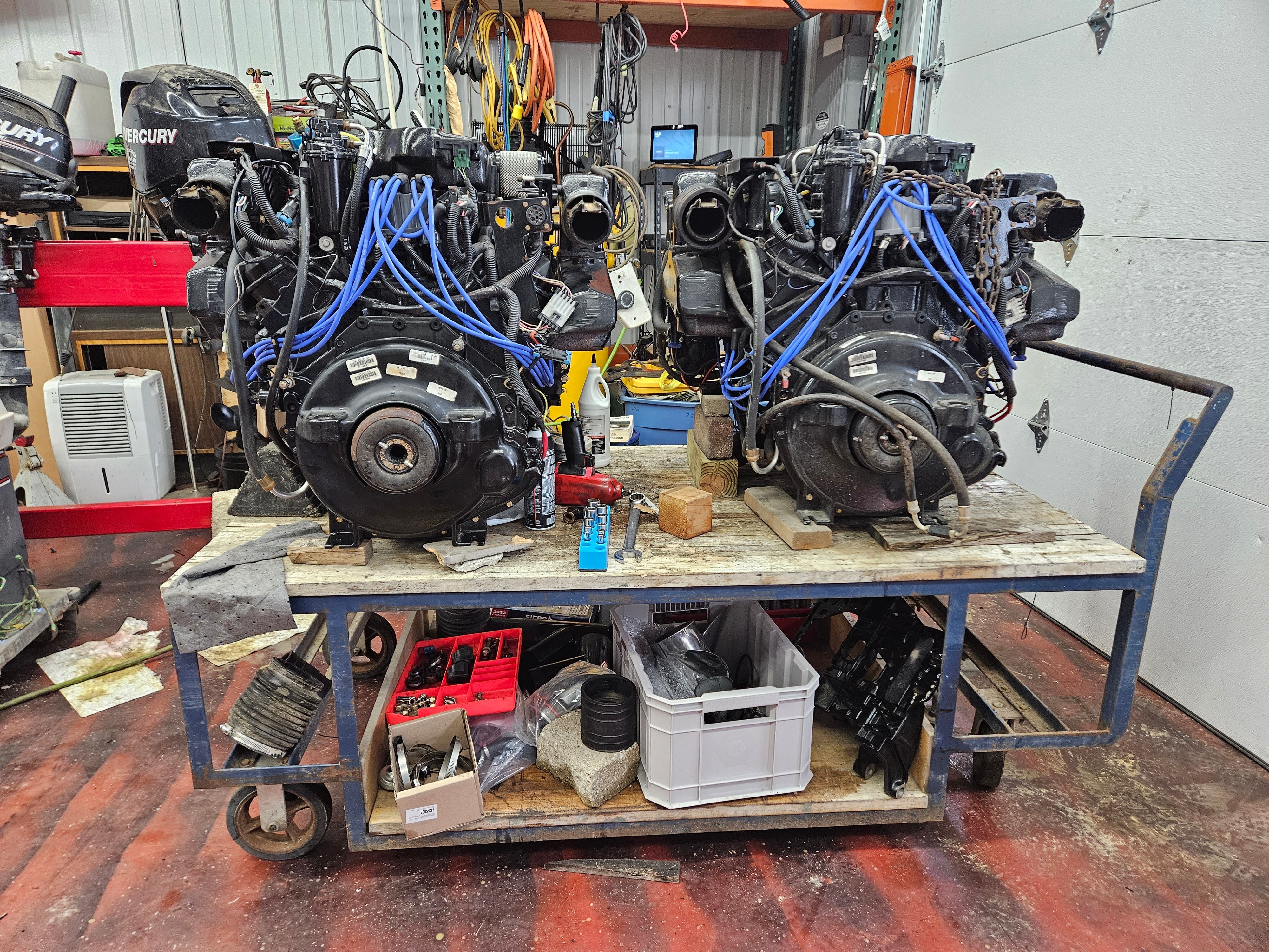 Two engines on a workshop cart with tools and spare parts underneath.