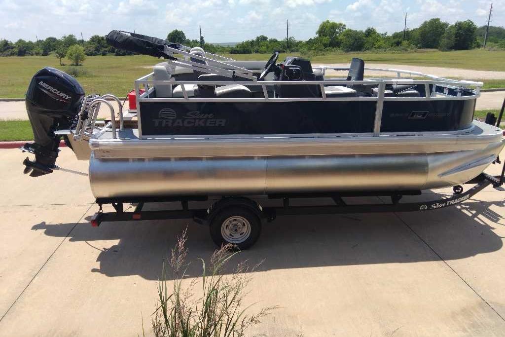 2026 Sun Tracker Bass Buggy 16 XL Select pontoon boat on trailer, parked outdoors.