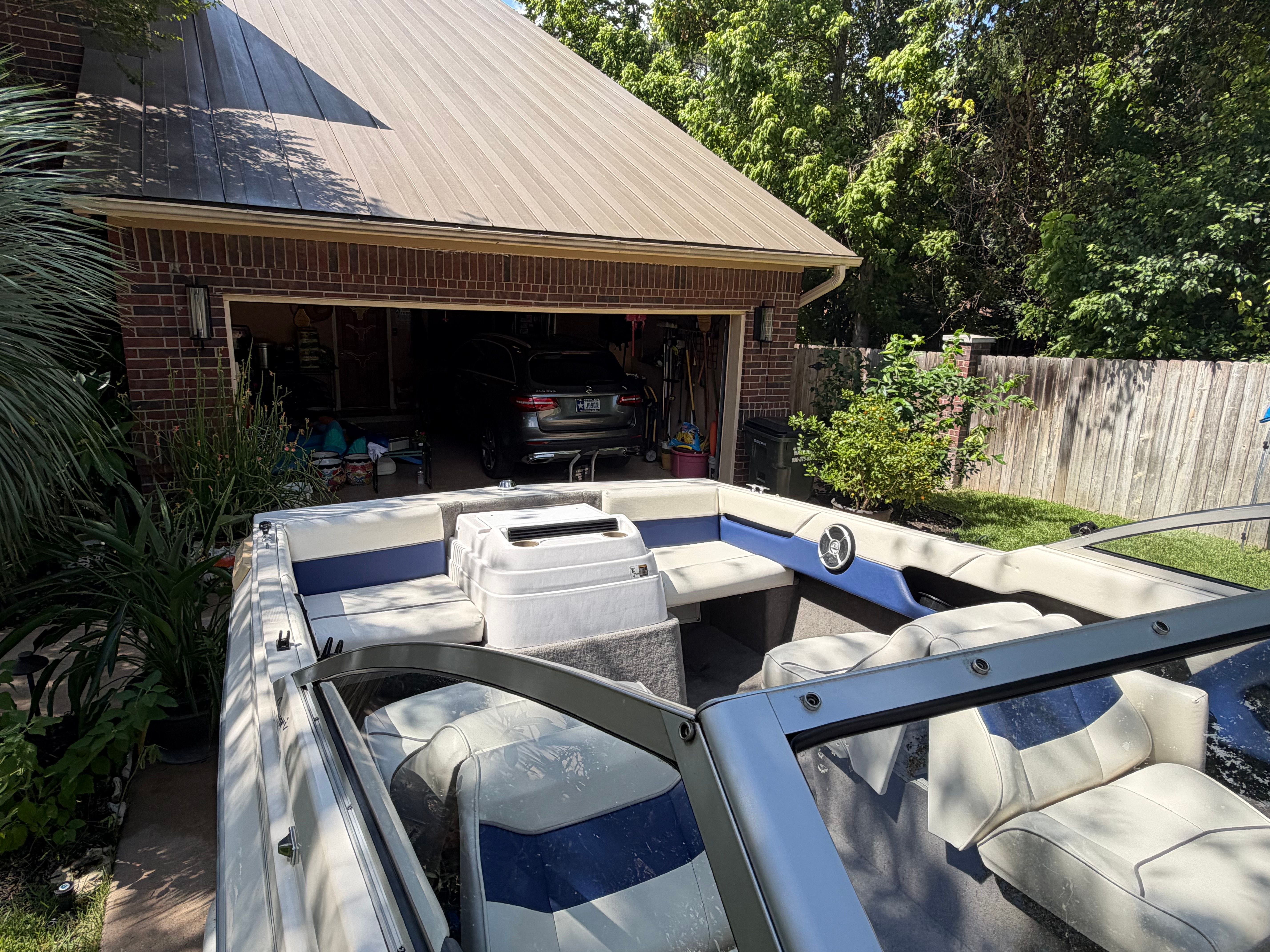 A 1994 Bayliner CAPRI is parked in a driveway in front of a garage. It has white and blue seats.