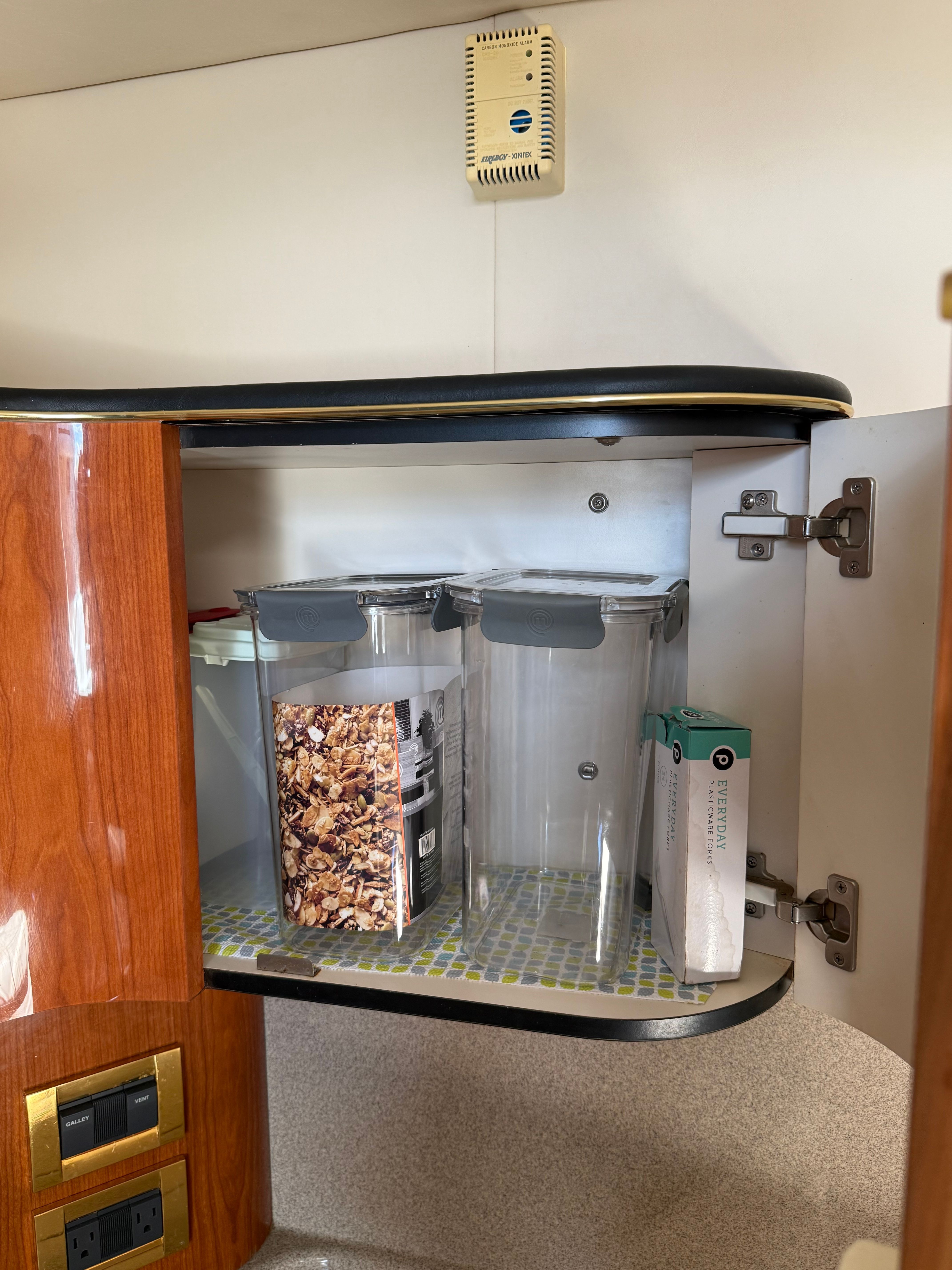 An open cabinet on a boat with storage containers and a cereal box.