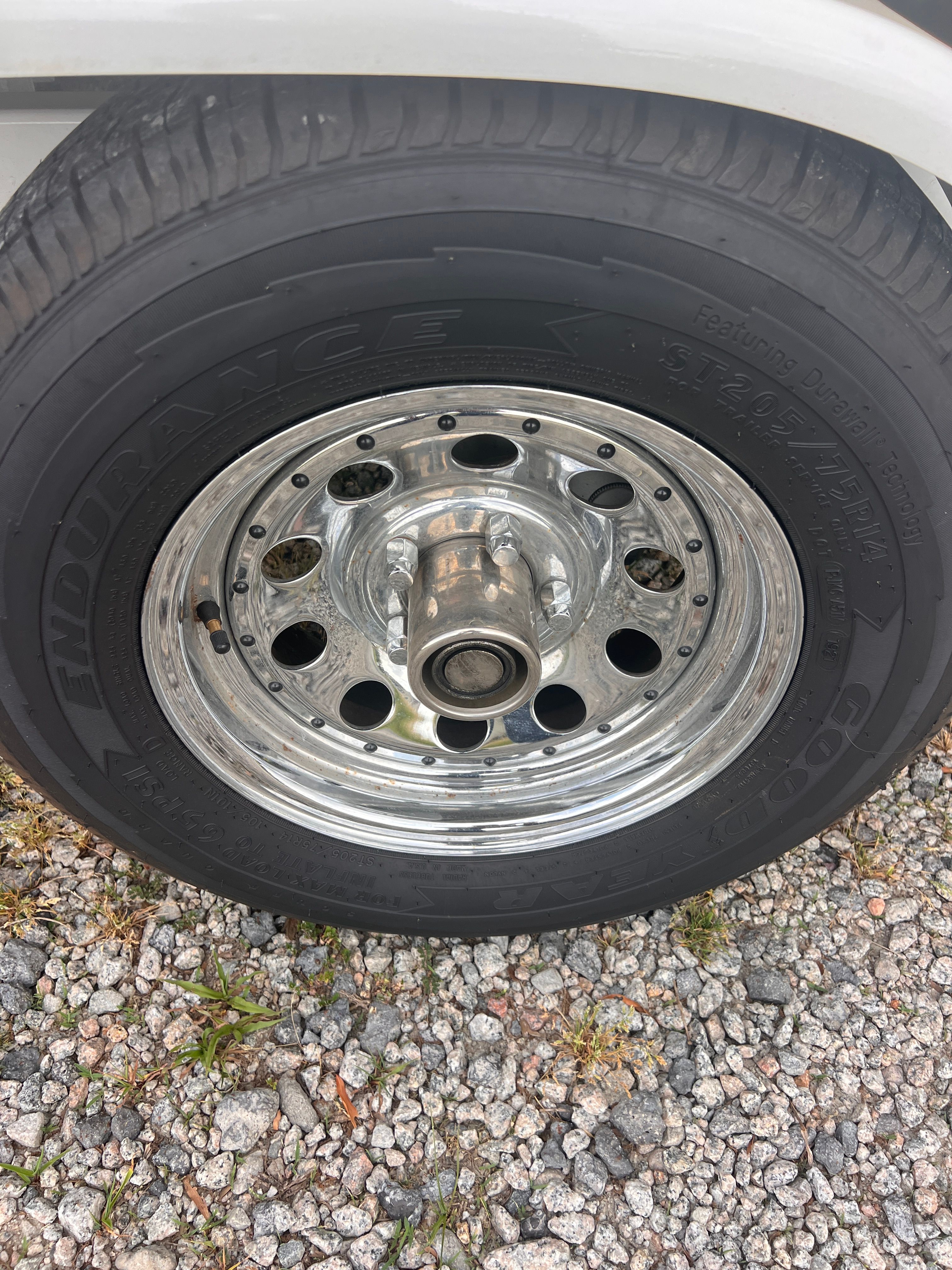 Close-up of a shiny metal wheel with a black tire on gravel.