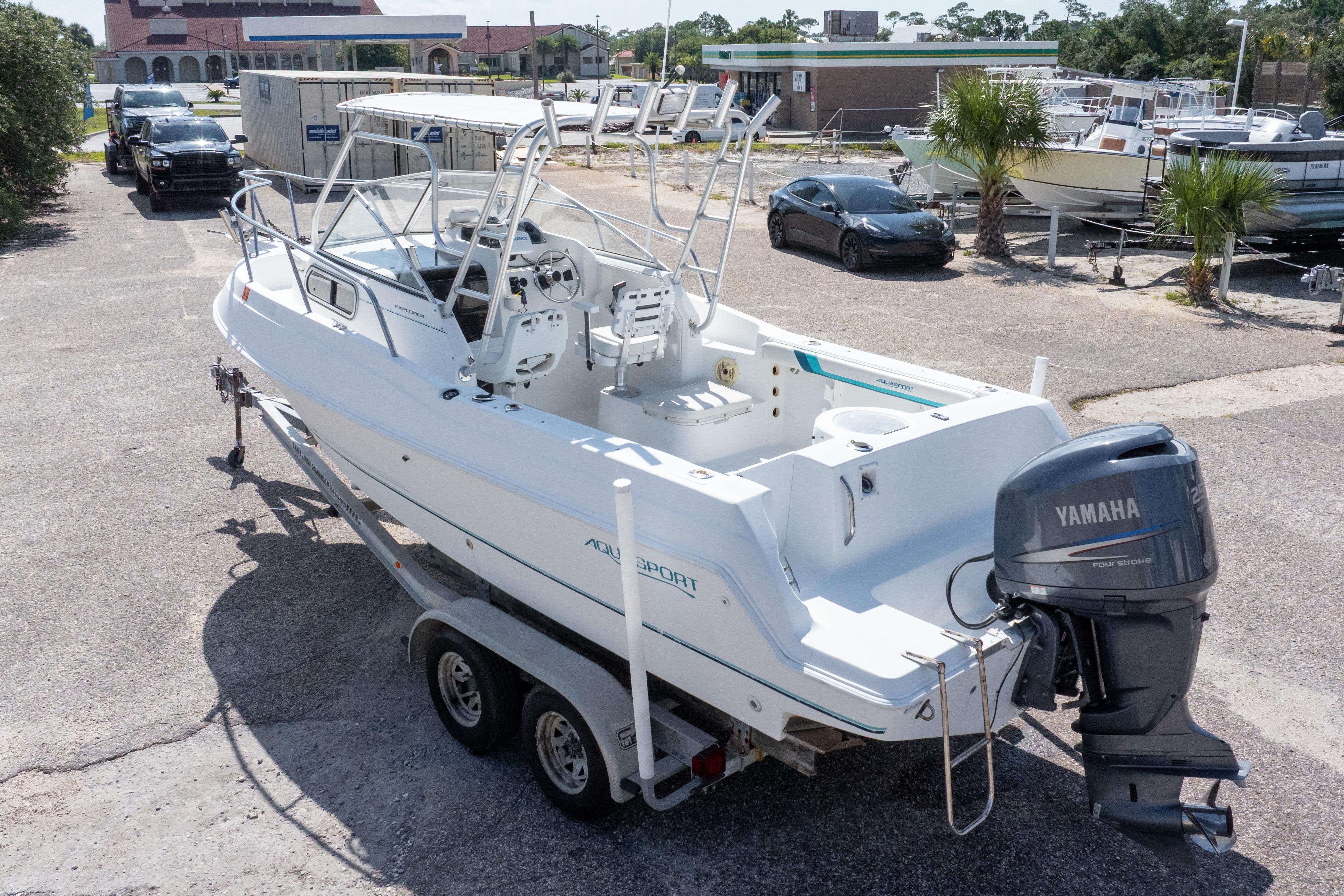 1999 Aquasport 225 Explorer boat with Yamaha engine on trailer in marina parking lot.