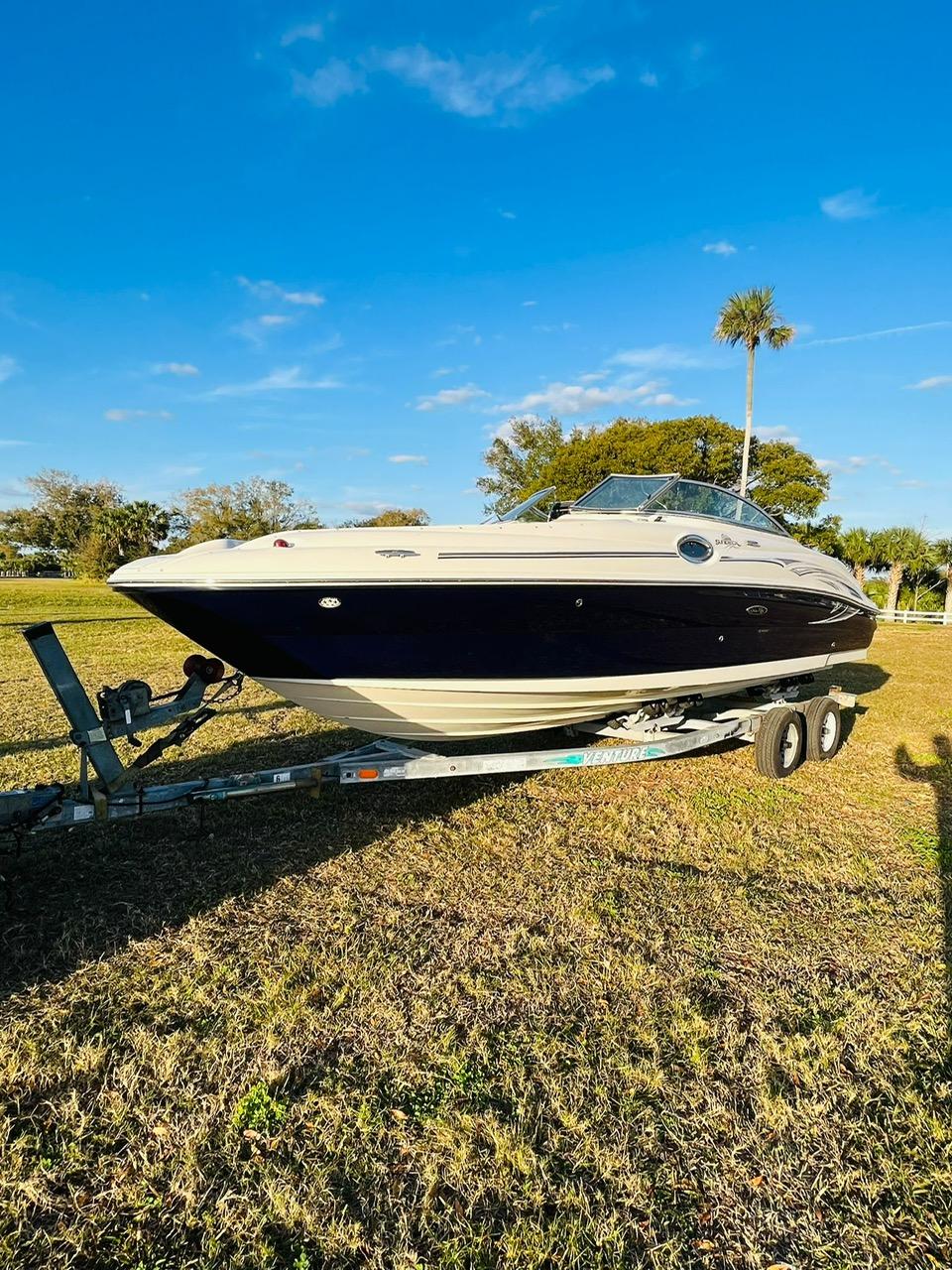 2005 Sea Ray 240 Sundeck boat on trailer, parked on grassy field under blue sky.