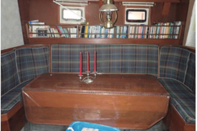 Cozy interior of 1997 Hike Metal Products ketch with plaid seating and bookshelves.