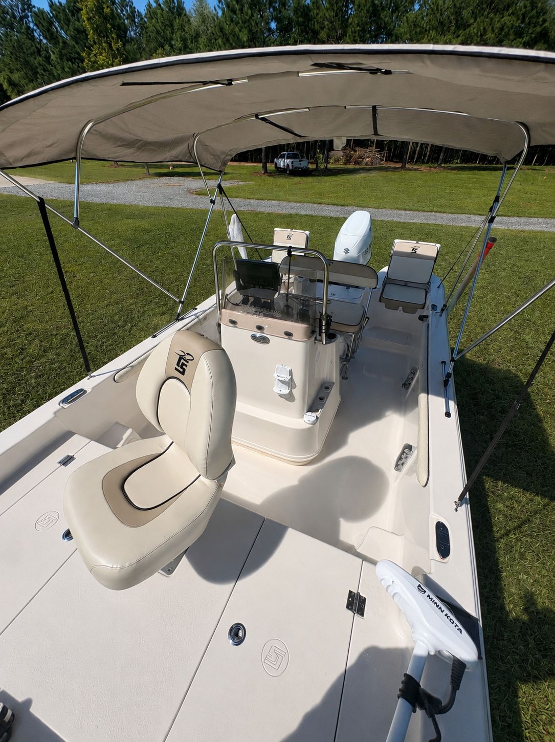 A 2022 Carolina Skiff 17 LS boat with a canopy and beige seats on a grassy area.