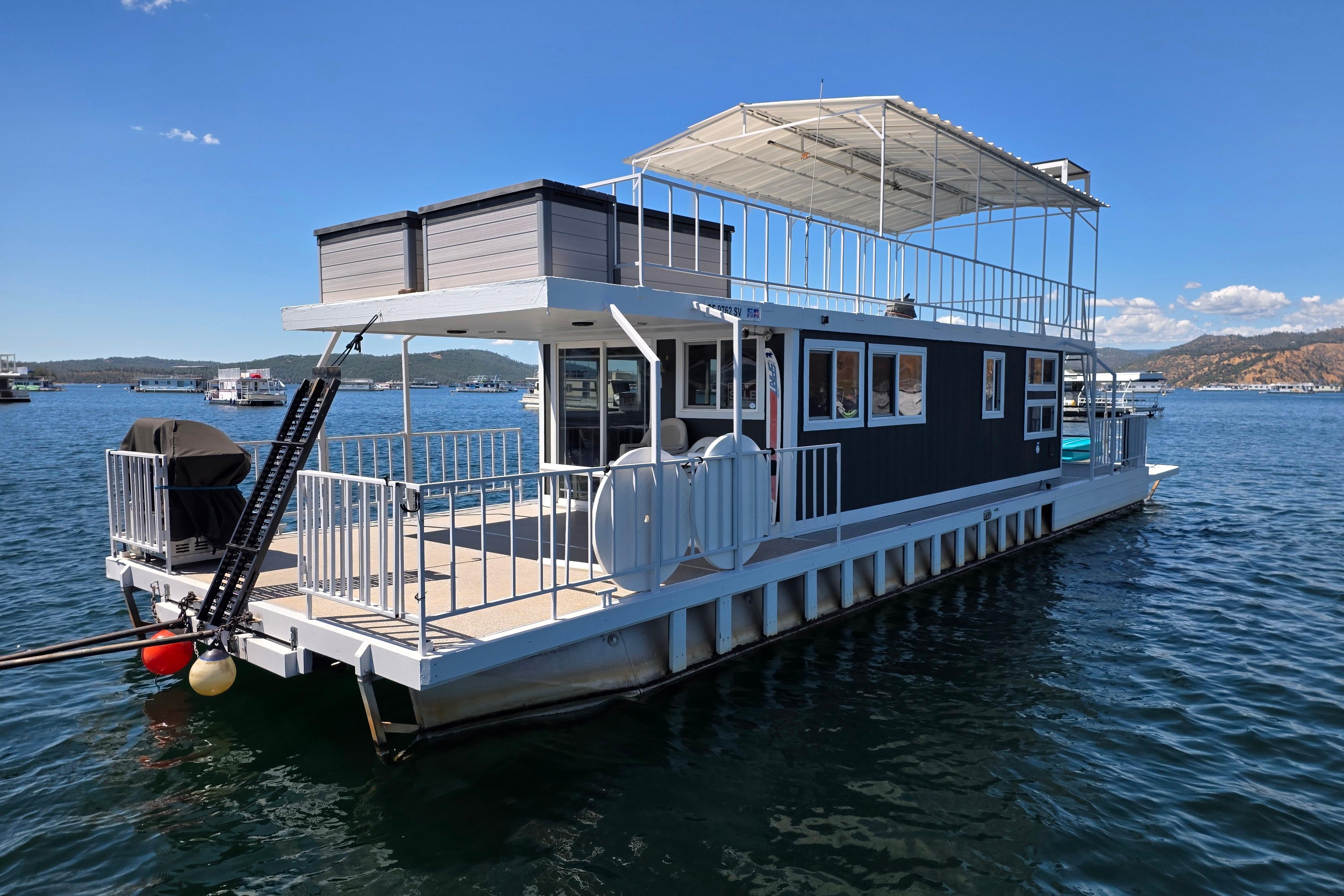 Custom 2007 houseboat on serene lake with upper deck and scenic mountain backdrop.