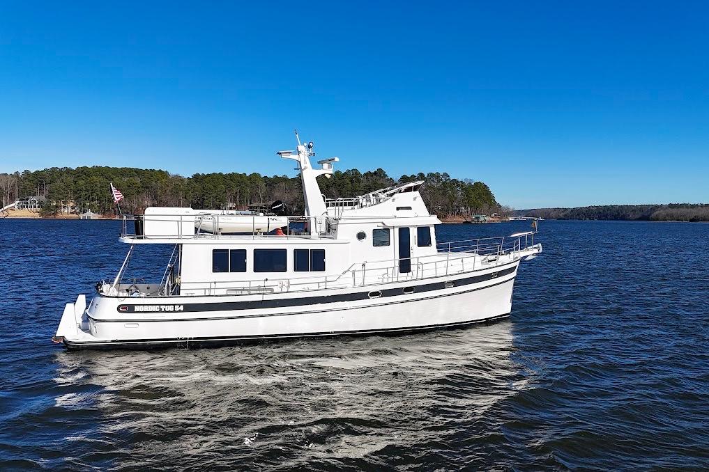 2007 Nordic Tug 54 cruising on a serene lake under a clear blue sky.